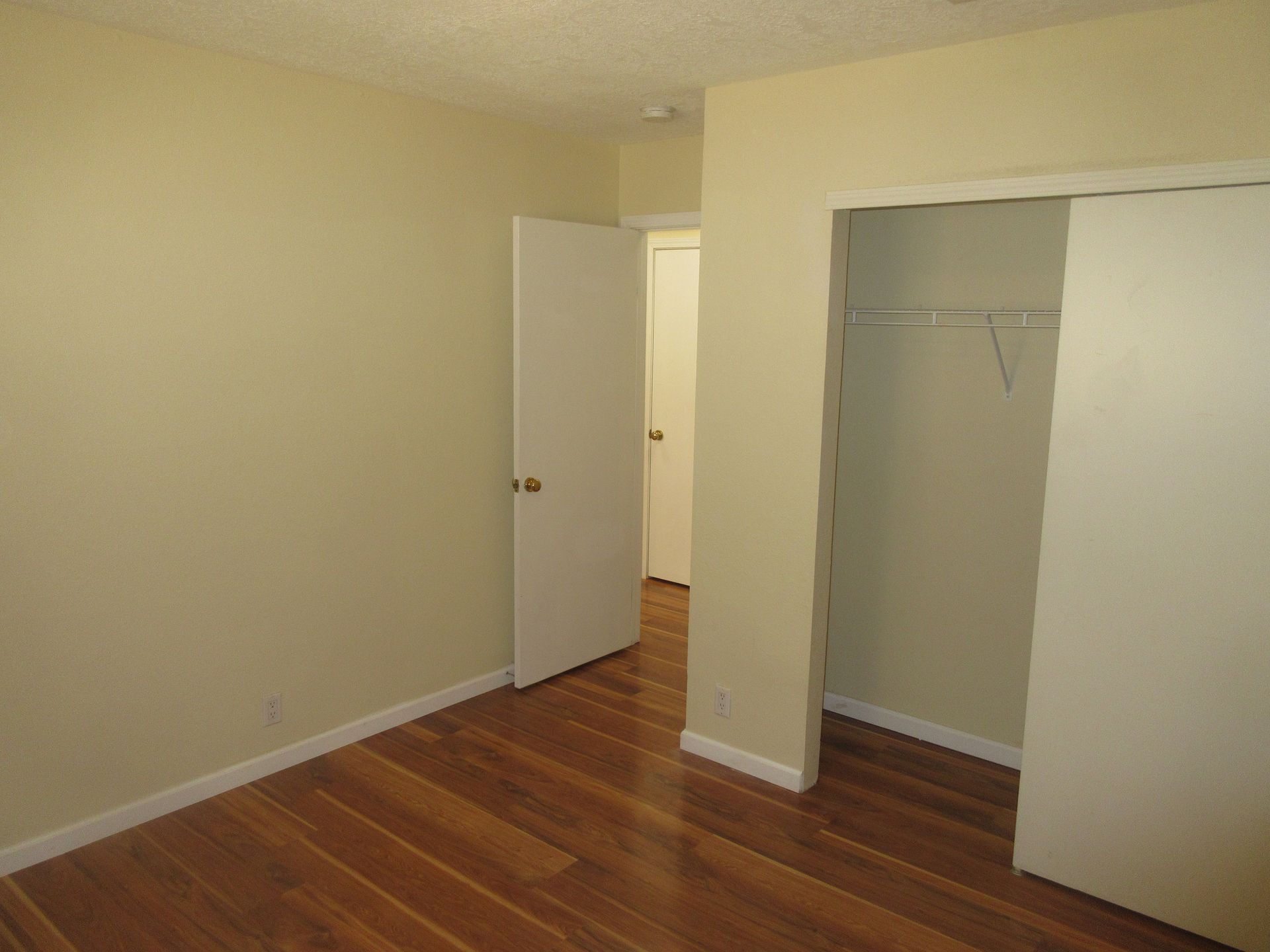 An empty bedroom with hardwood floors and a closet.