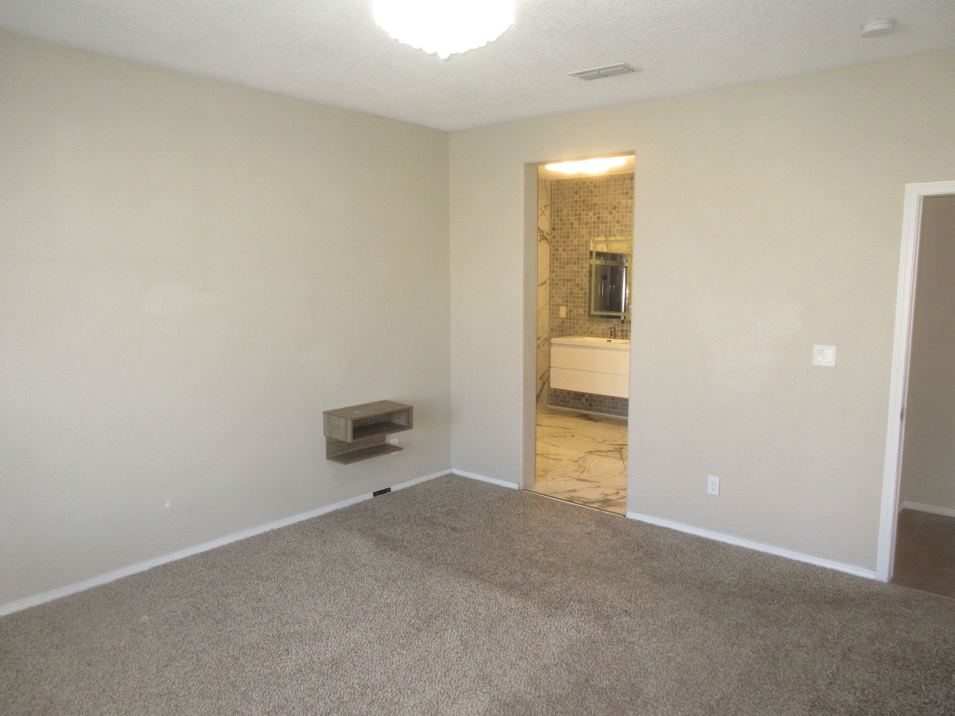 An empty bedroom with a carpeted floor and a door leading to a bathroom.