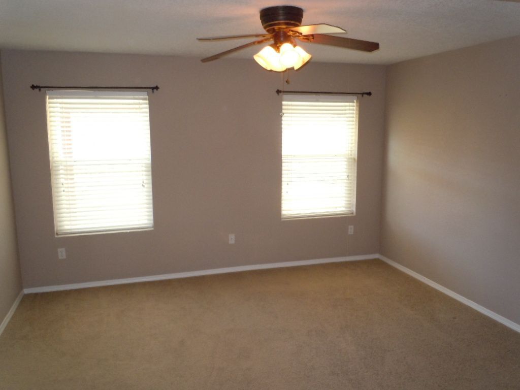 An empty room with two windows and a ceiling fan