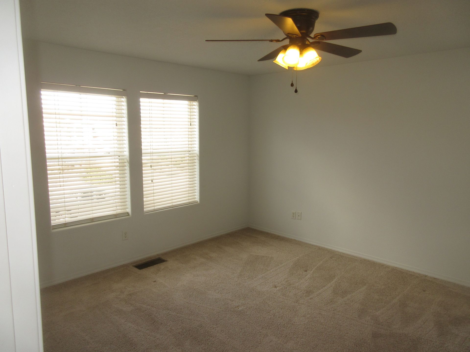 An empty bedroom with a ceiling fan and two windows