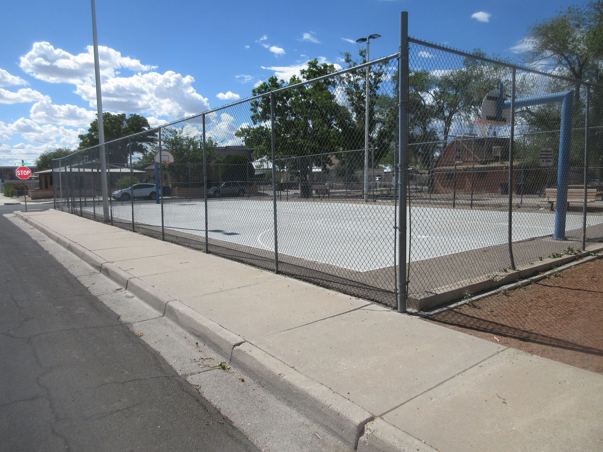 A basketball court is behind a chain link fence on the side of the road.