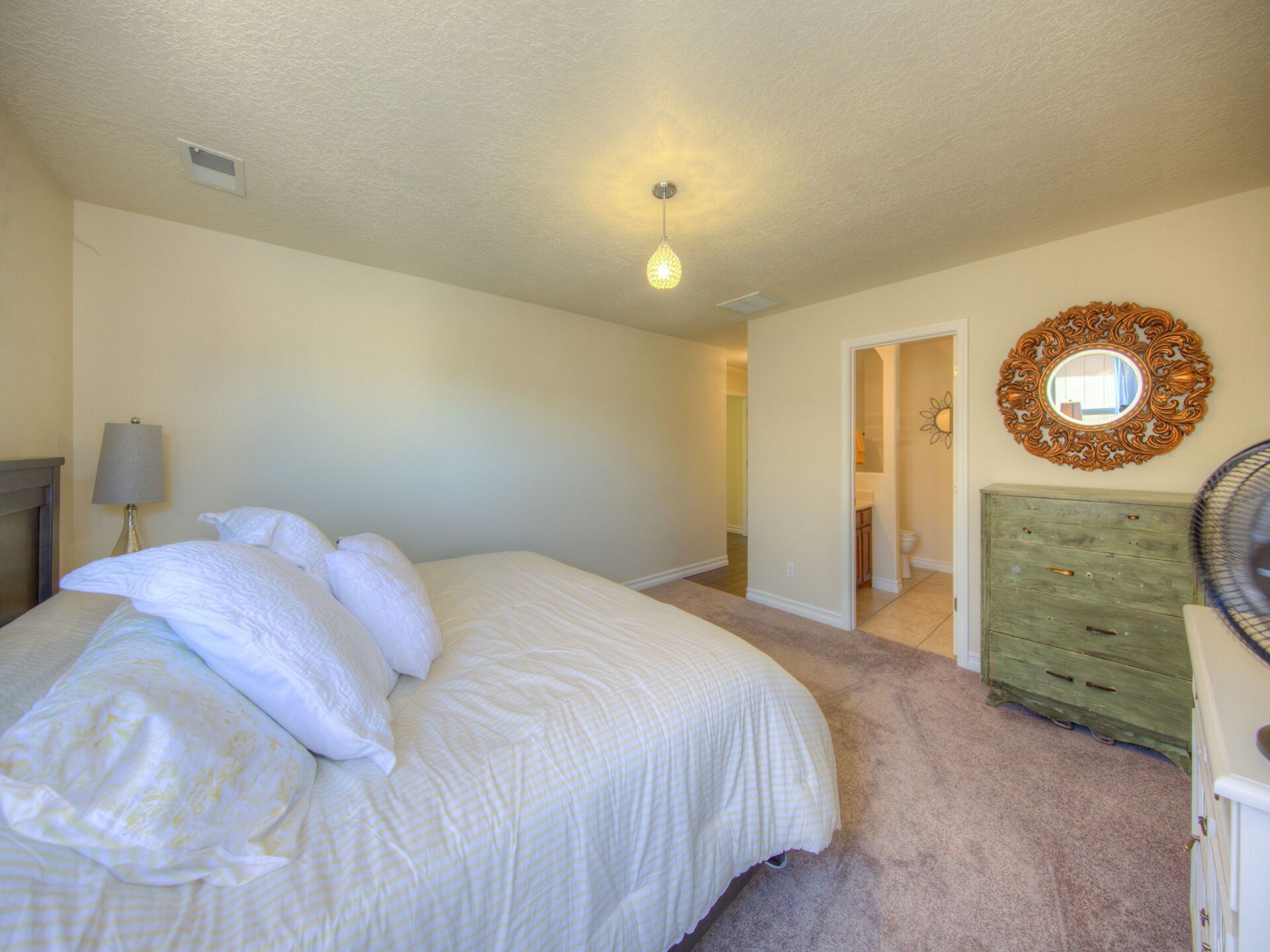 A bedroom with a bed , dresser , lamp and mirror.