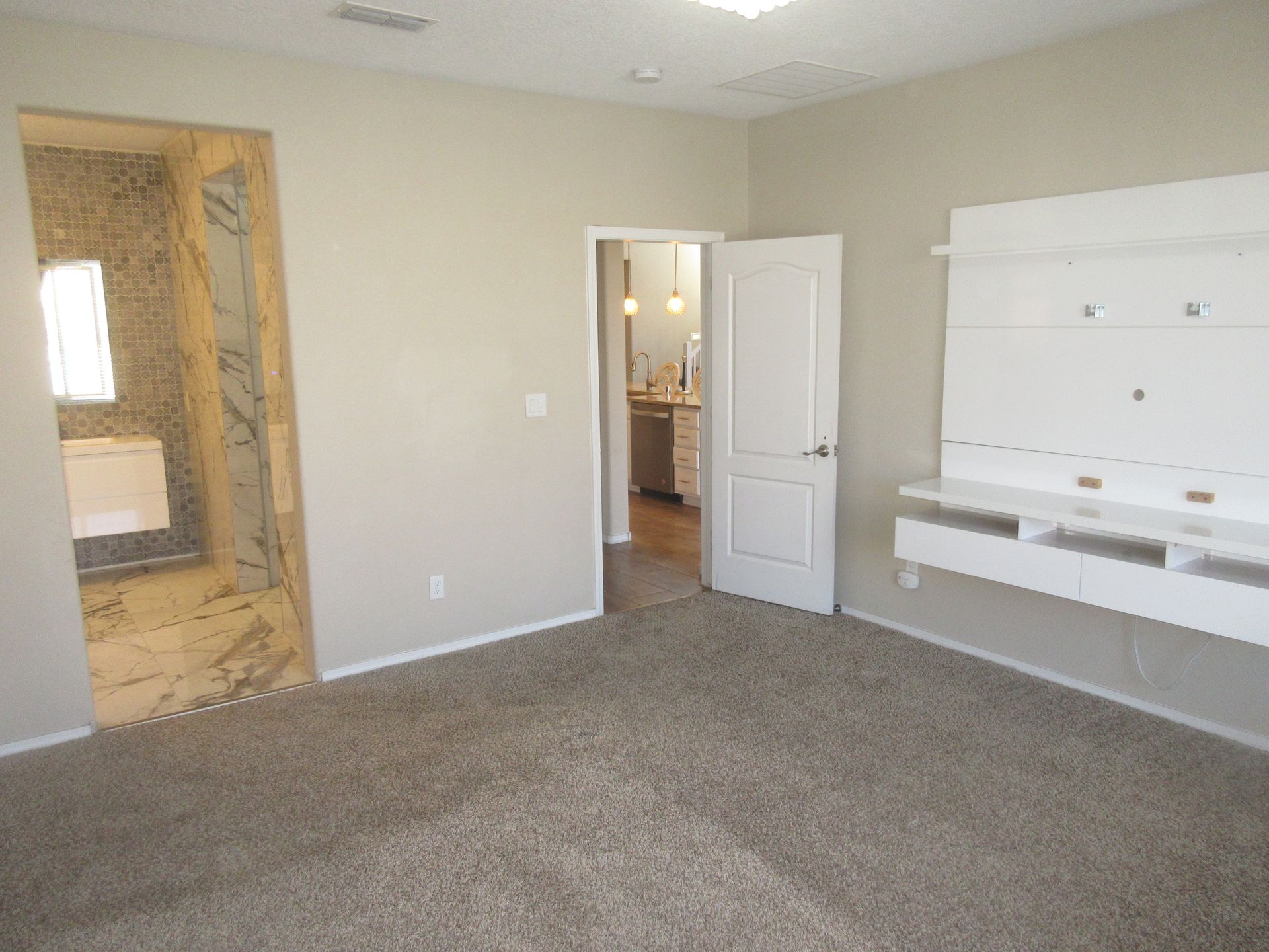 An empty room with a carpeted floor and a television mounted on the wall.