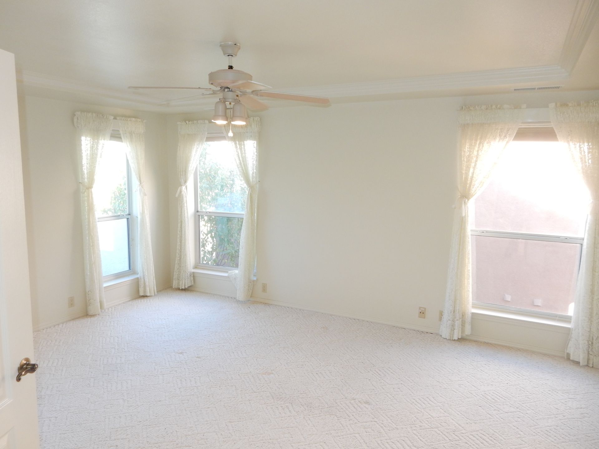 An empty bedroom with a ceiling fan and two windows.