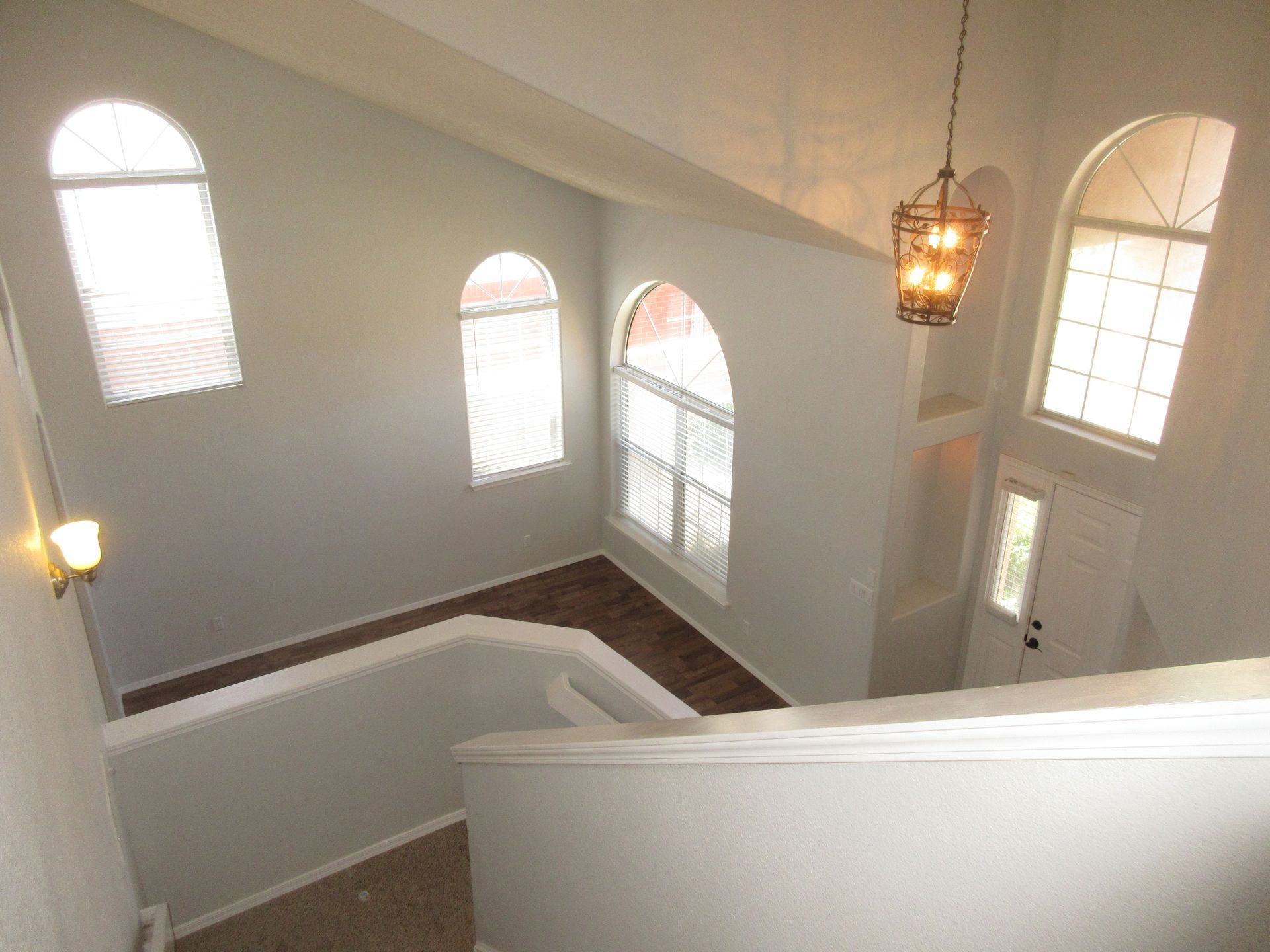 An aerial view of a staircase in a house with arched windows and a chandelier hanging from the ceiling.