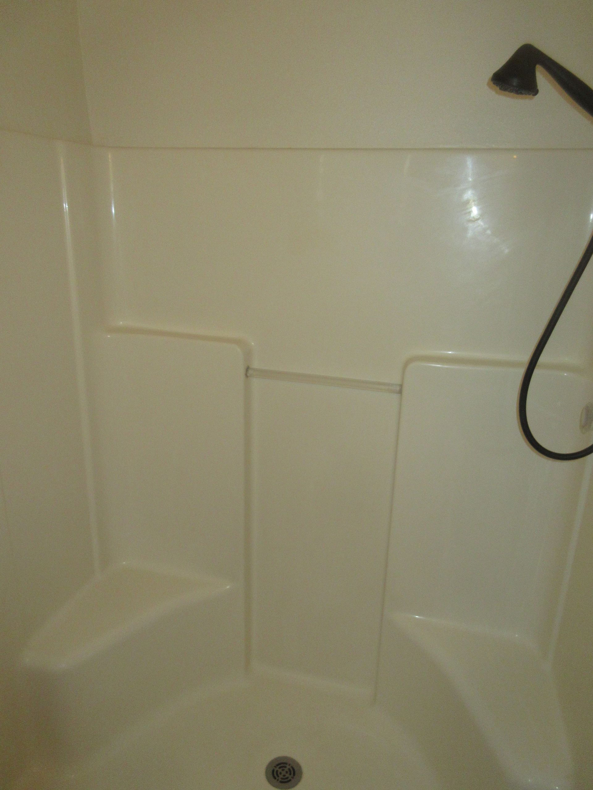 A white shower with a shower head and a drain