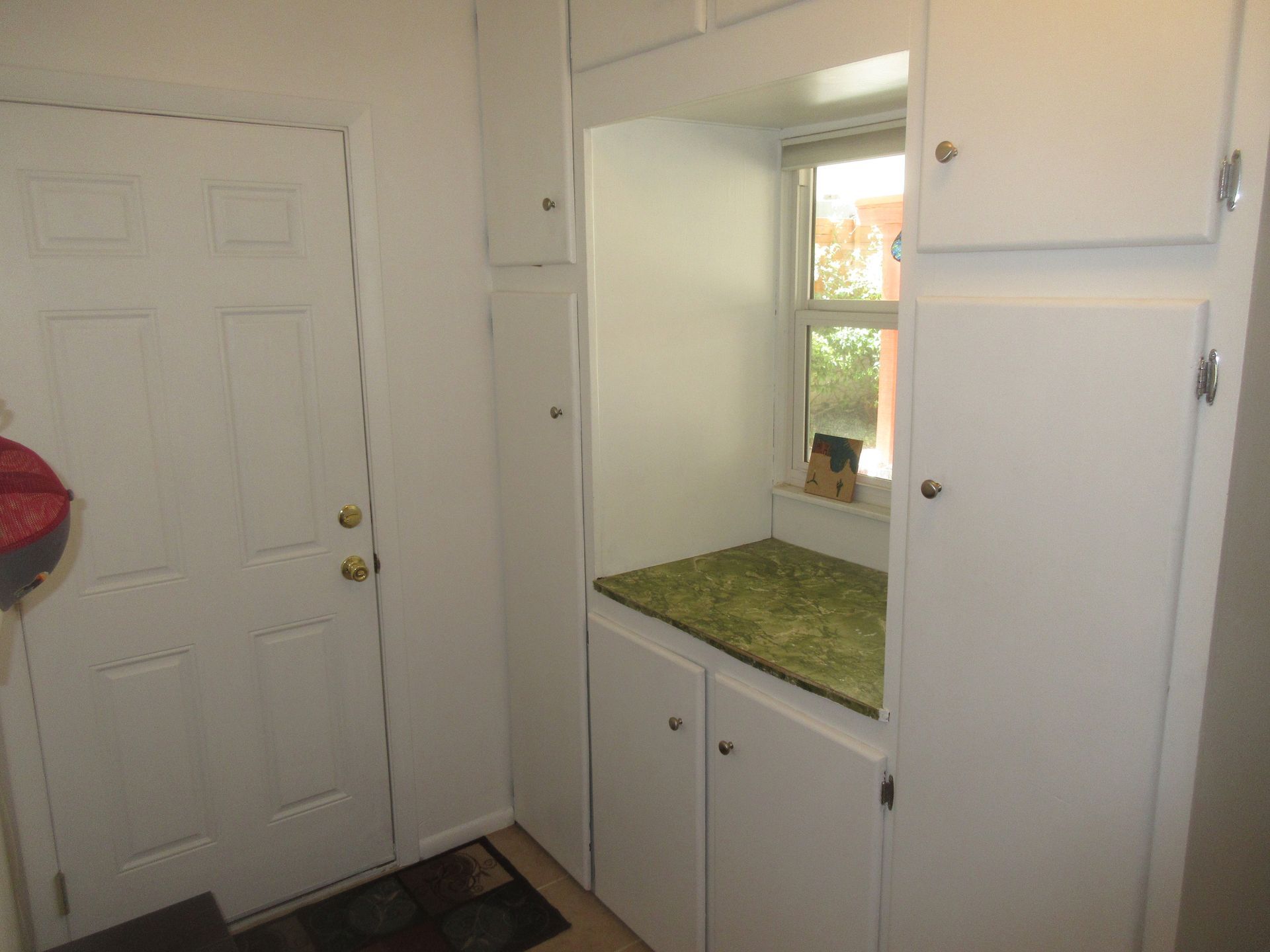 A laundry room with white cabinets and a window.