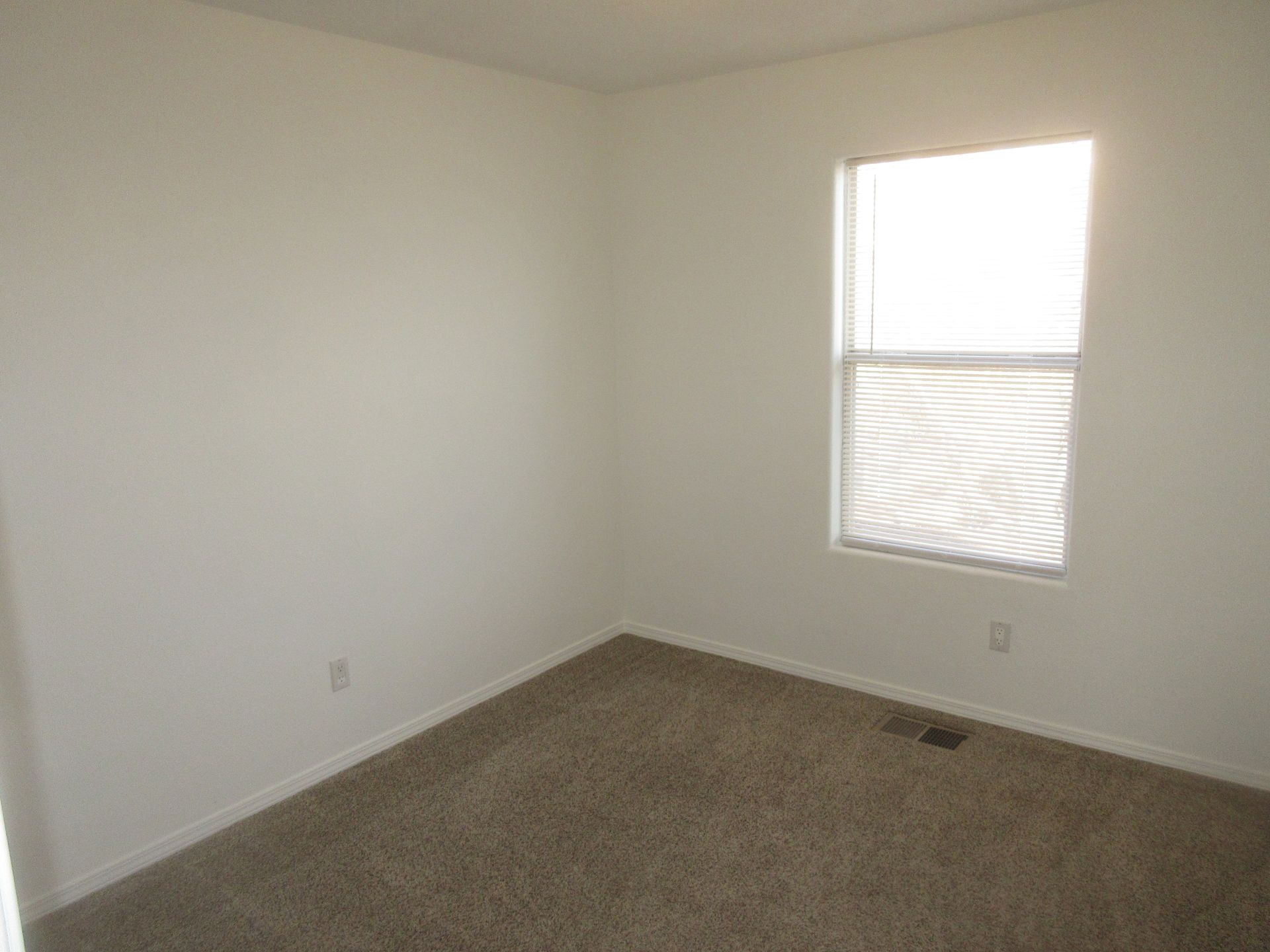 An empty bedroom with a window and carpet.