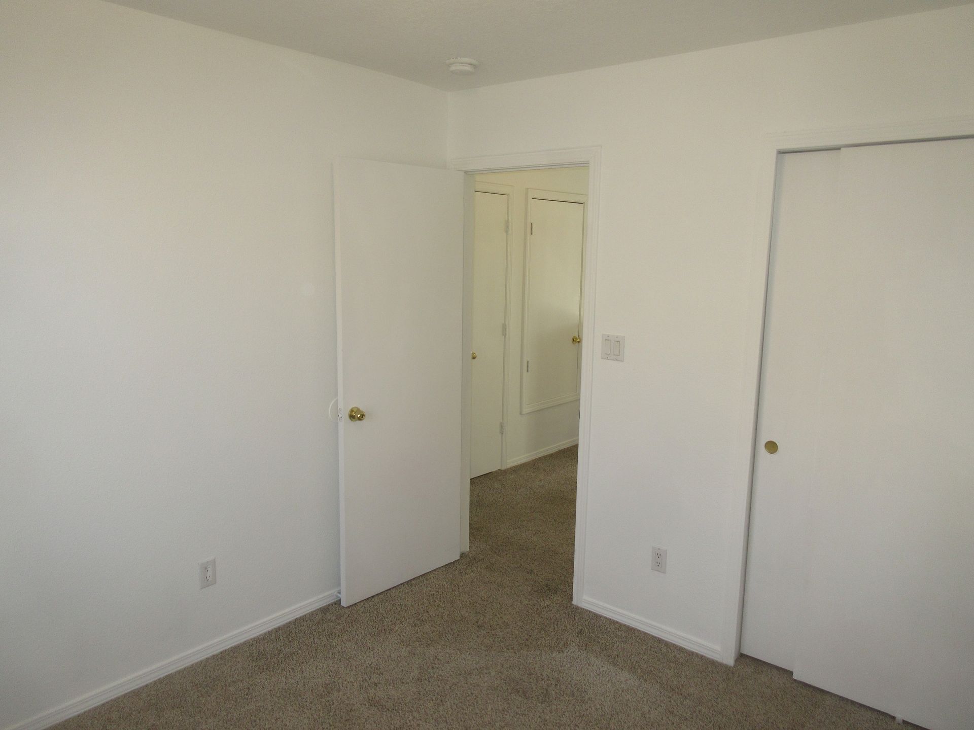 An empty bedroom with a carpeted floor and white walls.