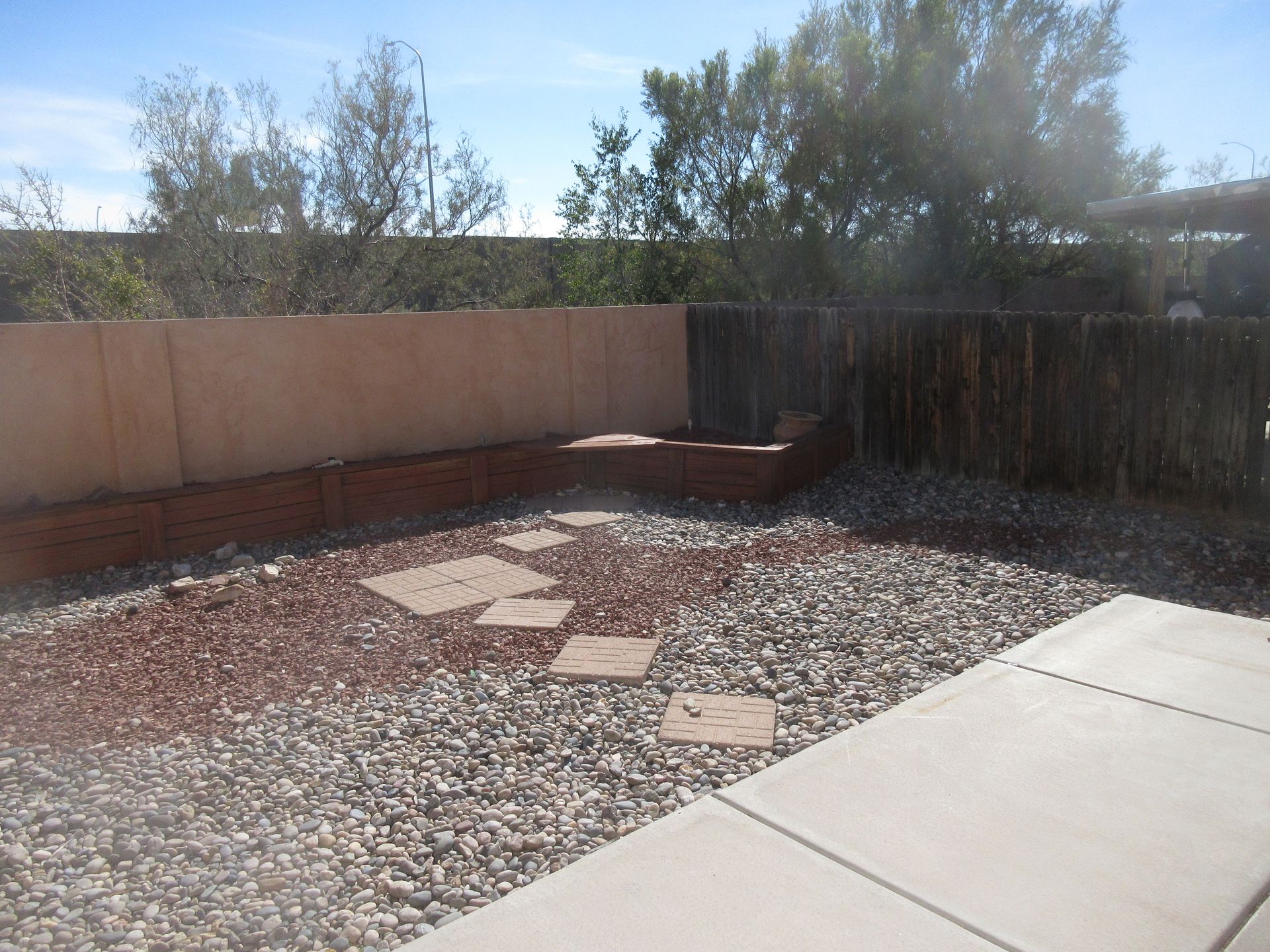 A gravel yard with a fence and trees in the background