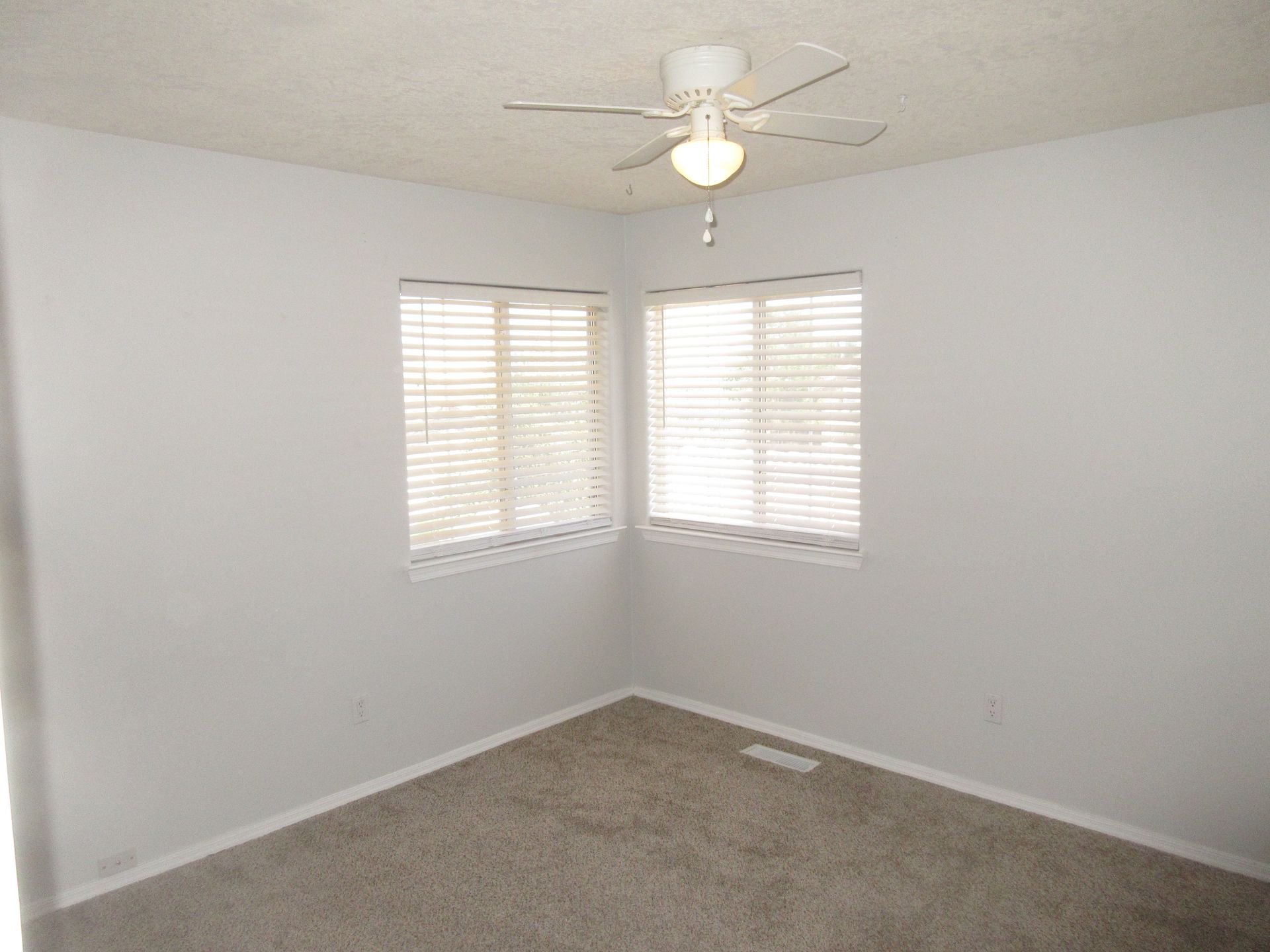 An empty bedroom with a ceiling fan and two windows.