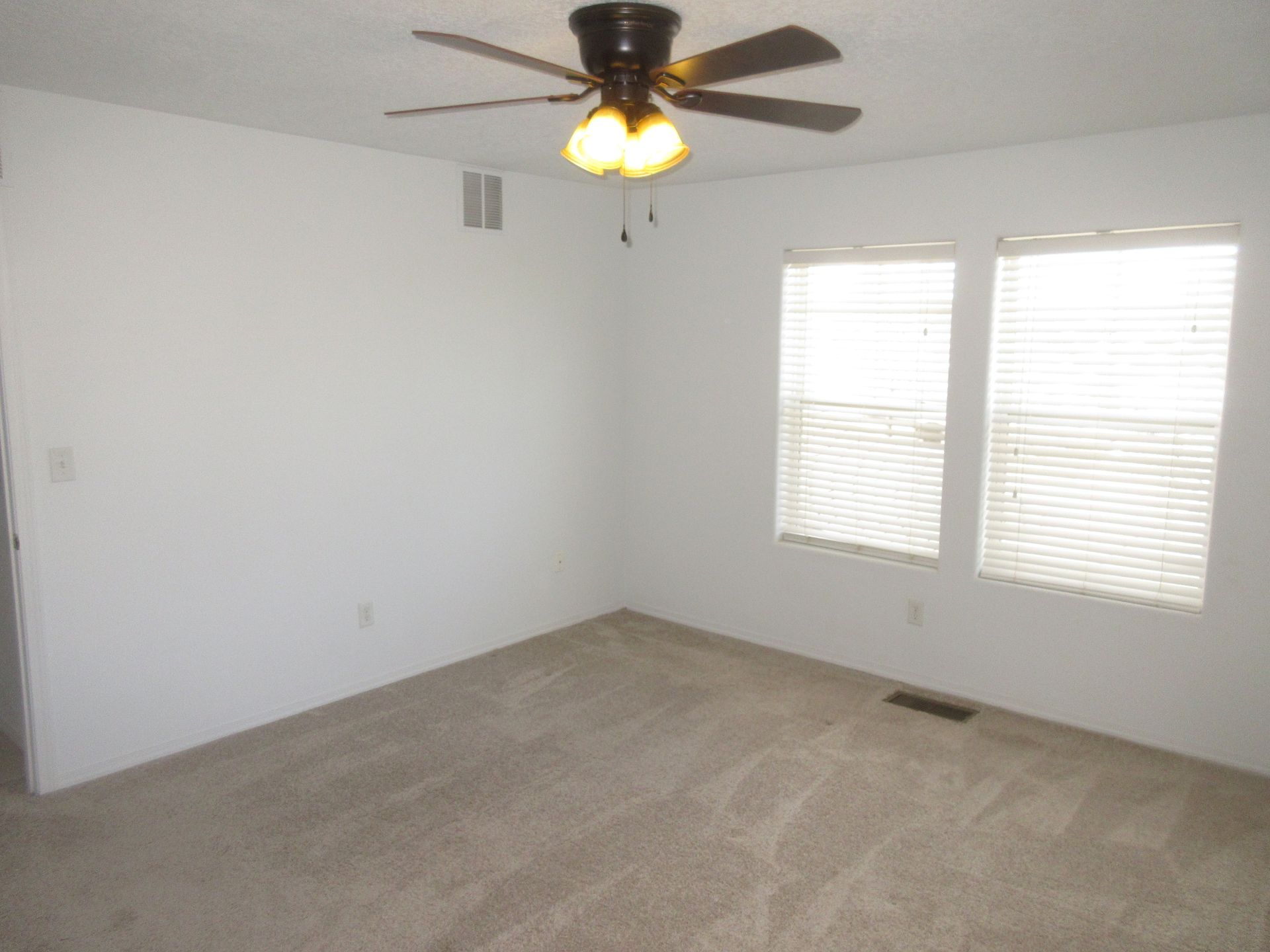 An empty room with a ceiling fan and two windows