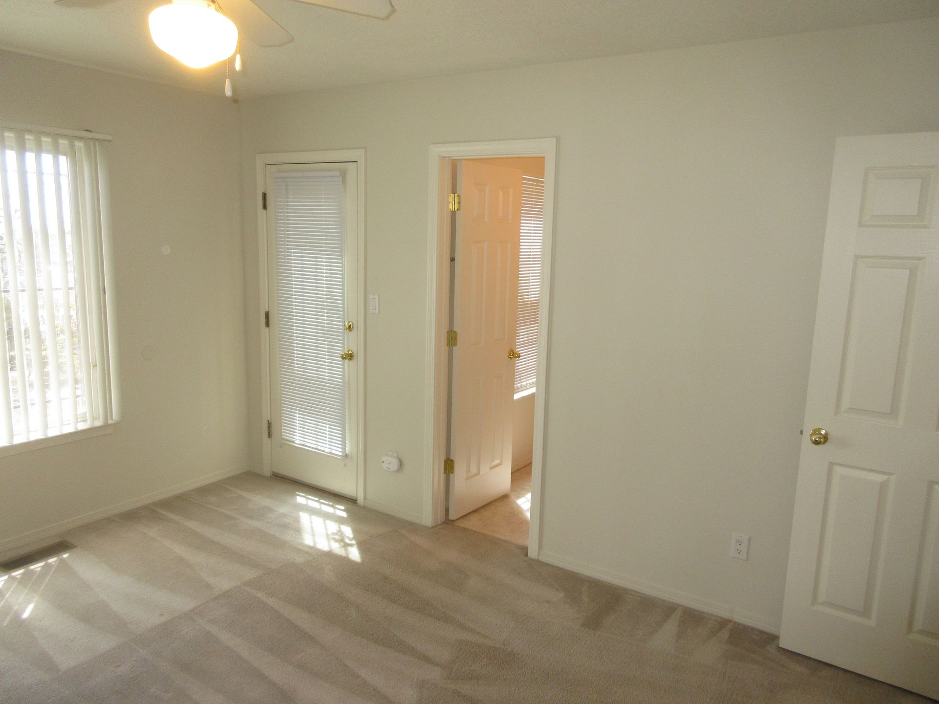 An empty room with a ceiling fan and a sliding glass door