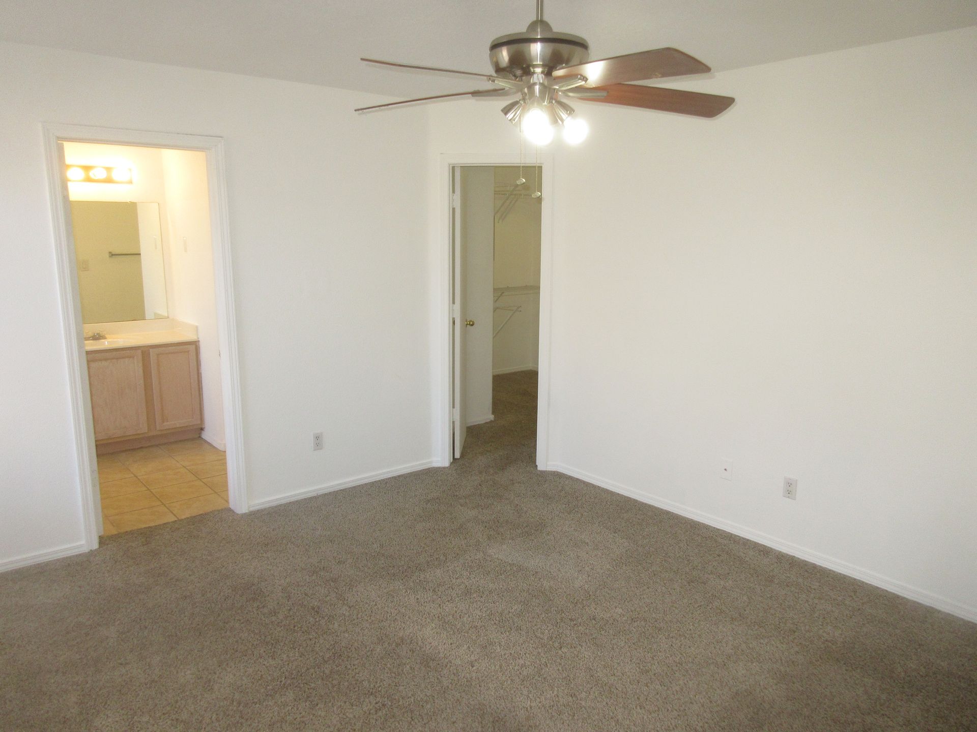 An empty bedroom with a ceiling fan and a bathroom