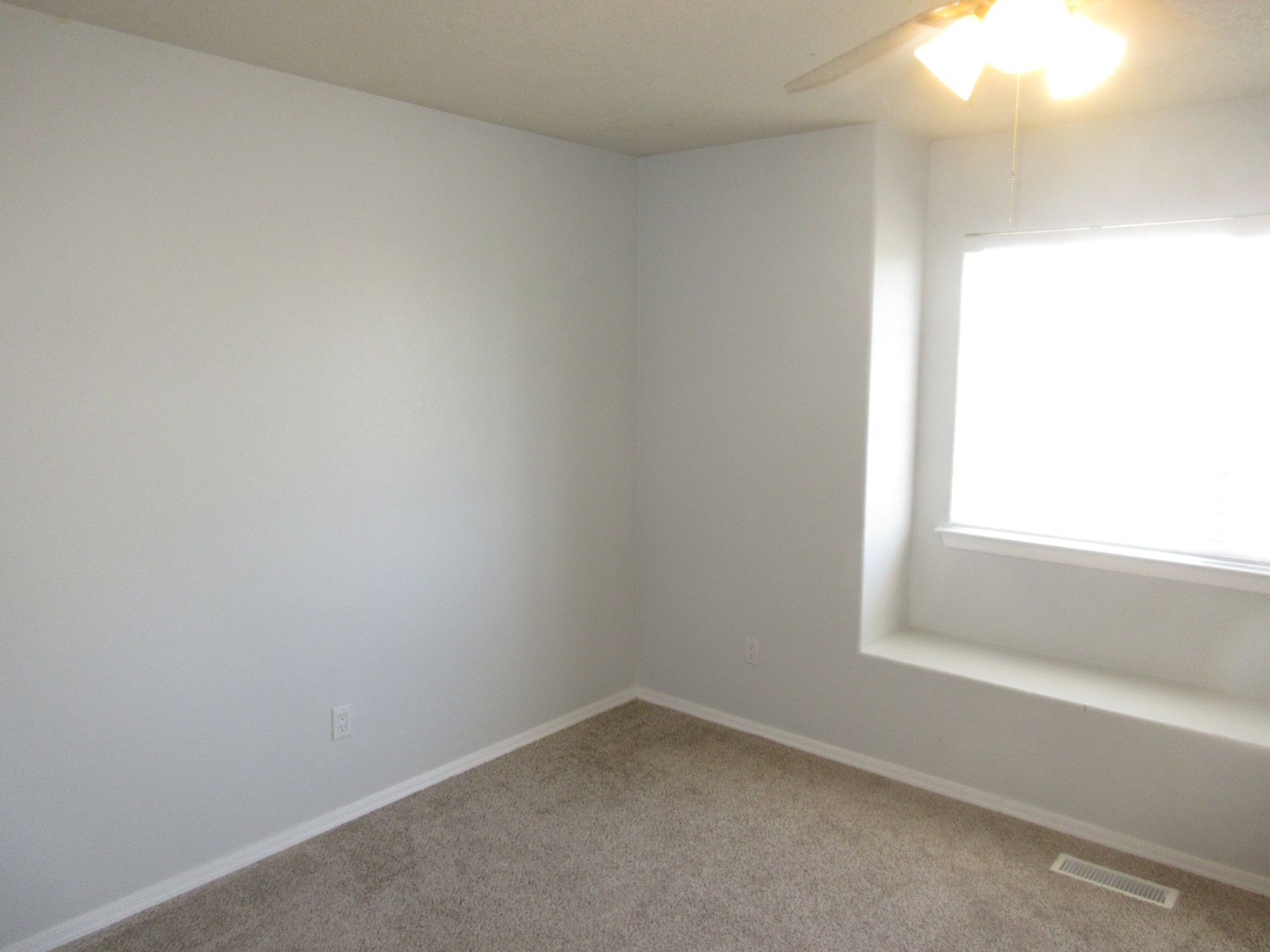 An empty bedroom with a window and a ceiling fan.
