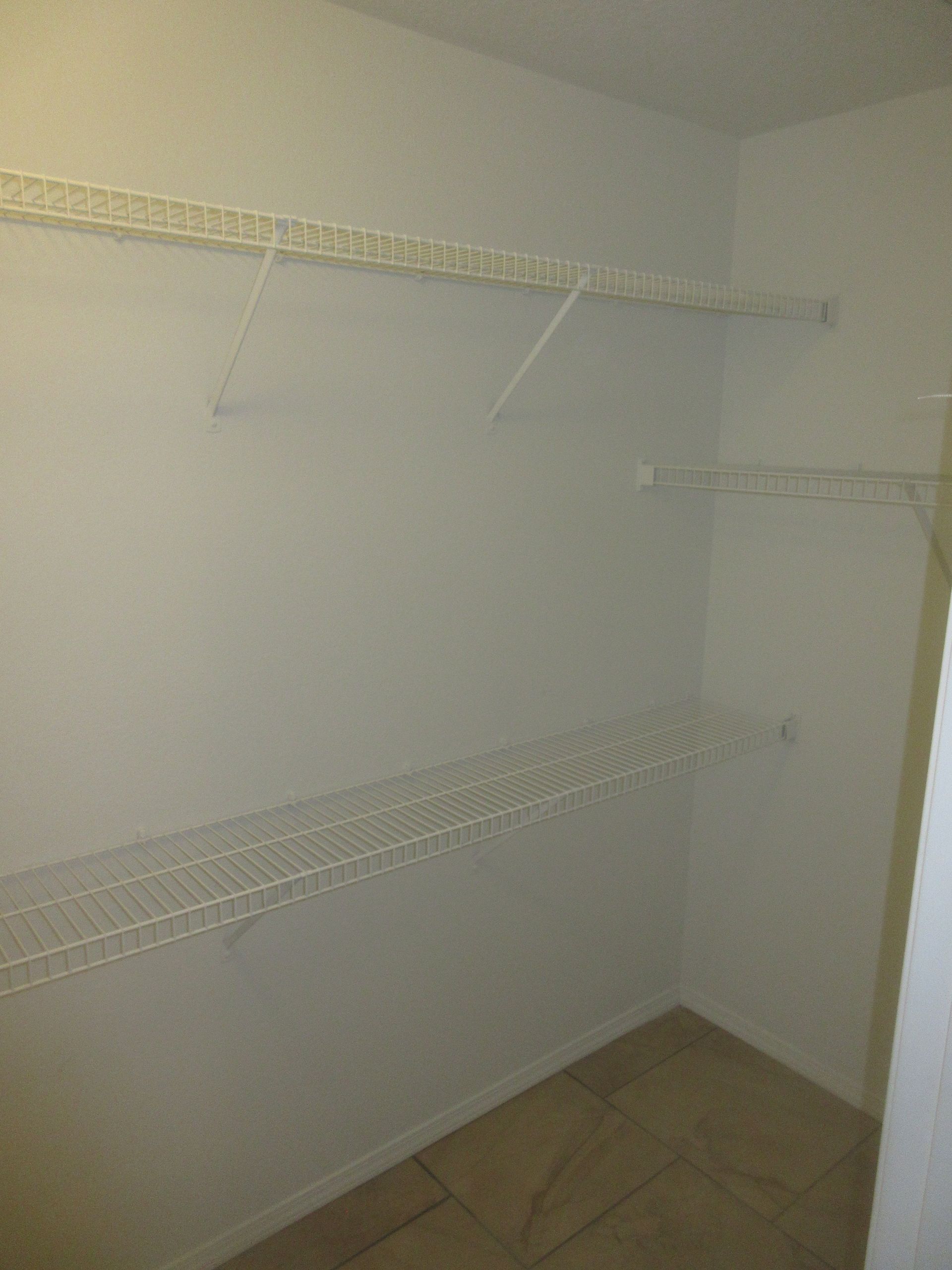 An empty walk in closet with white shelves and tile floors.