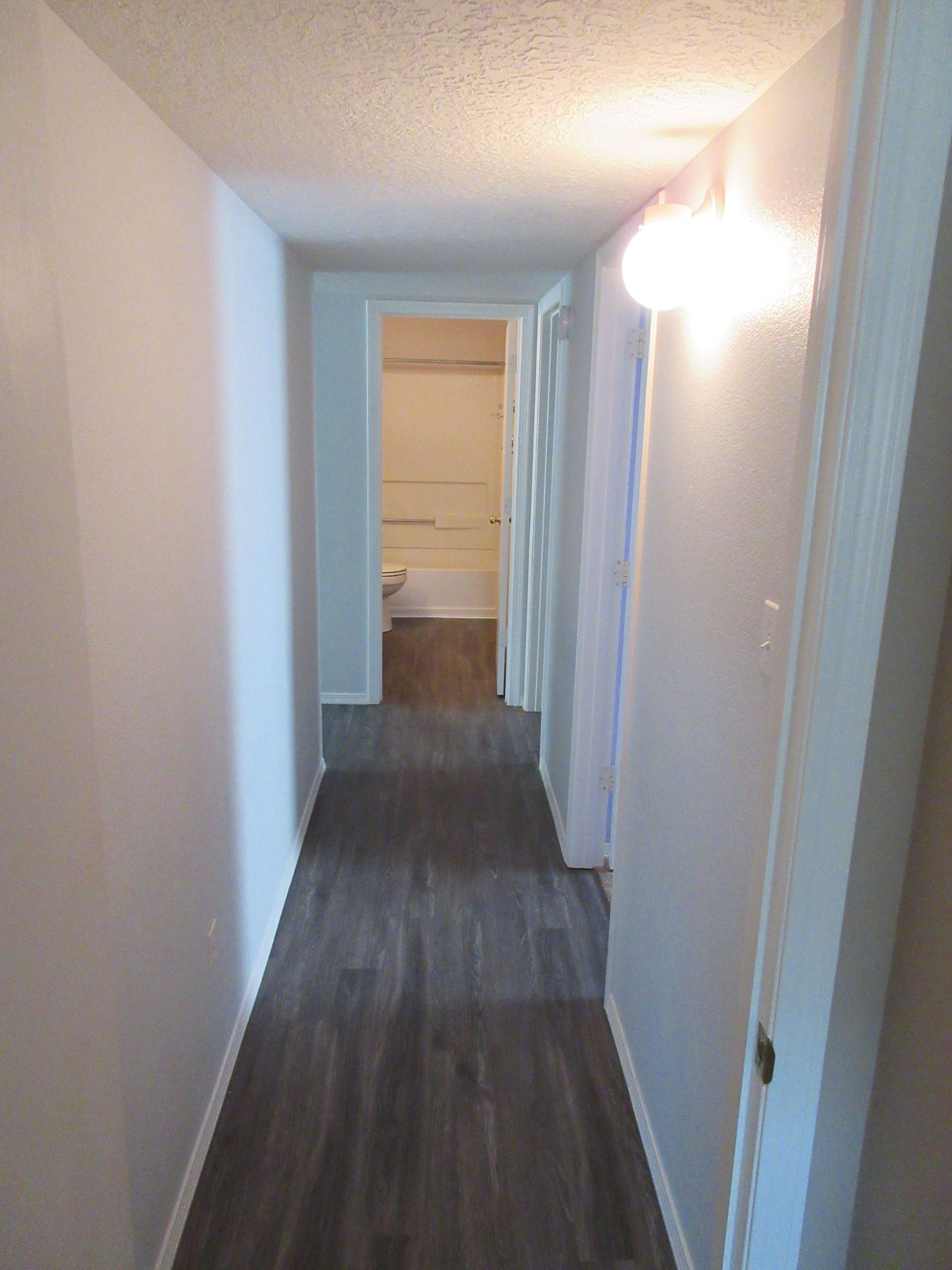 A long hallway with hardwood floors leading to a bathroom.