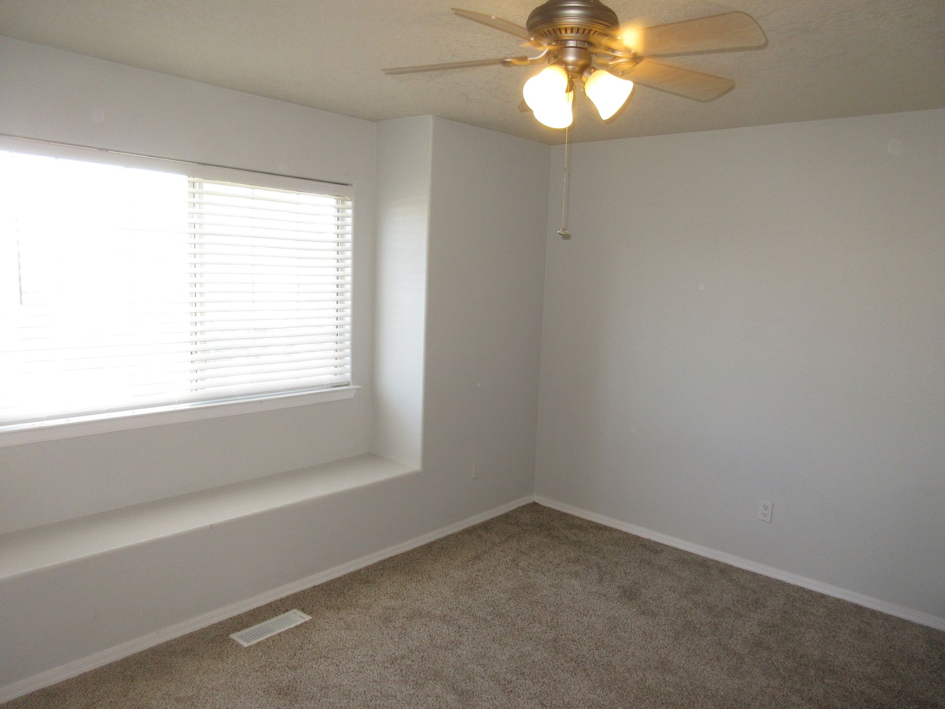 An empty bedroom with a ceiling fan and a window.