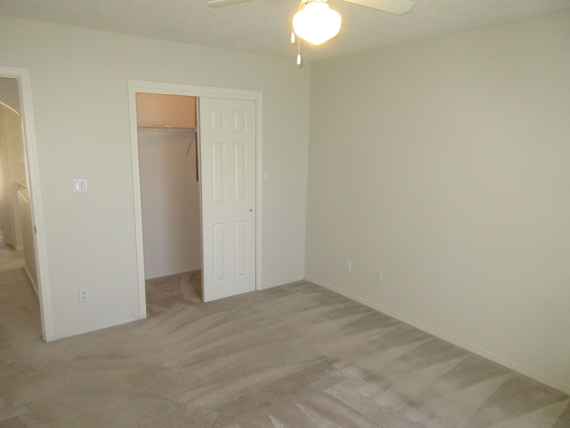 An empty bedroom with a ceiling fan and a closet.