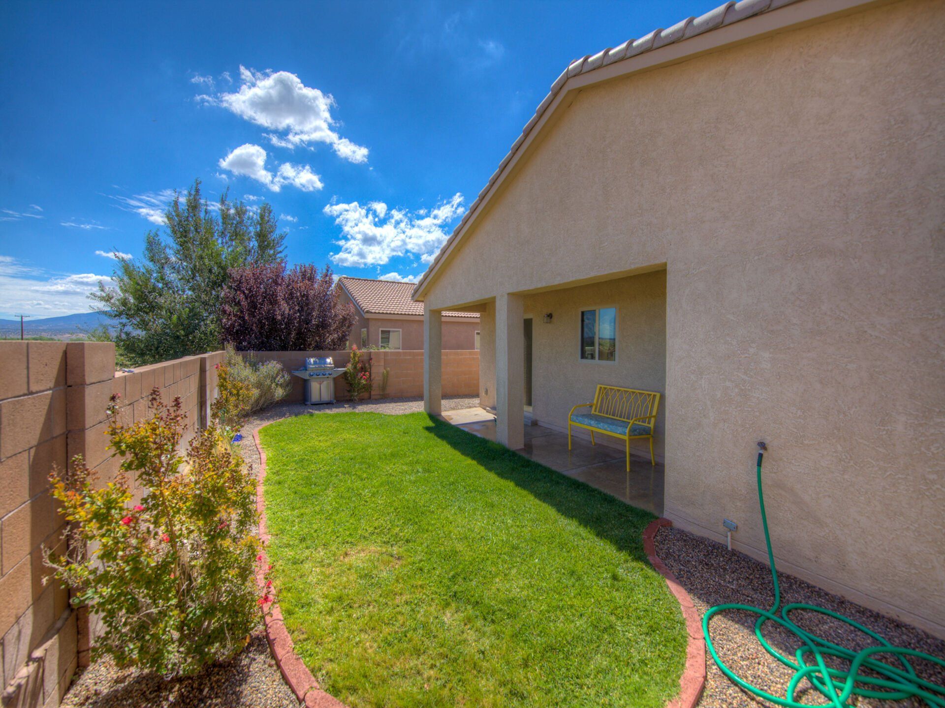 The backyard of a house with a large lawn and a green hose.