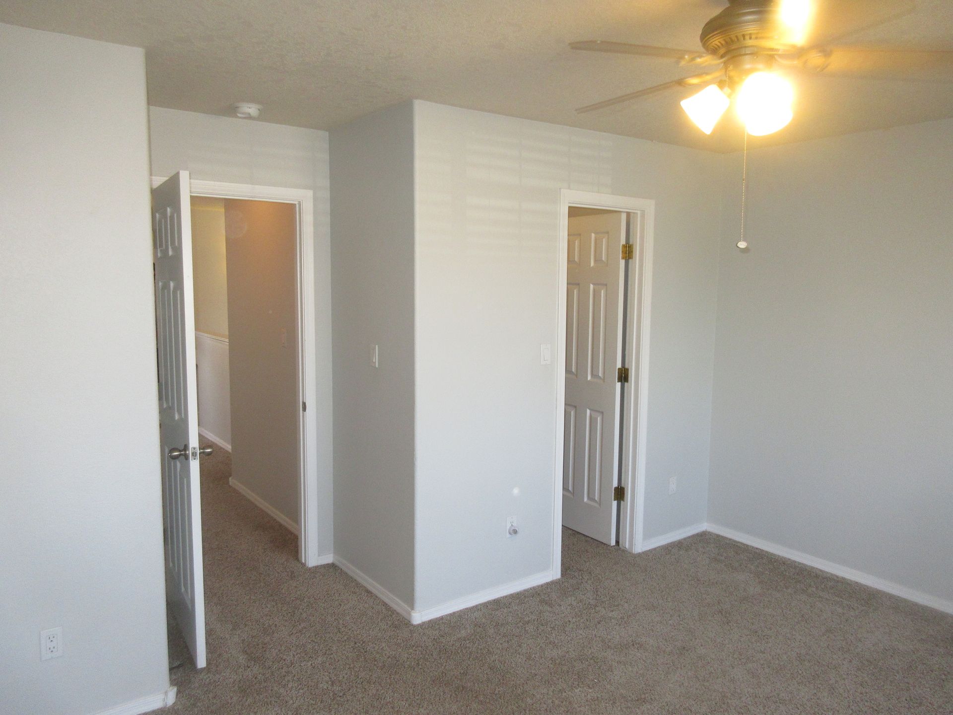 An empty bedroom with a ceiling fan and two doors