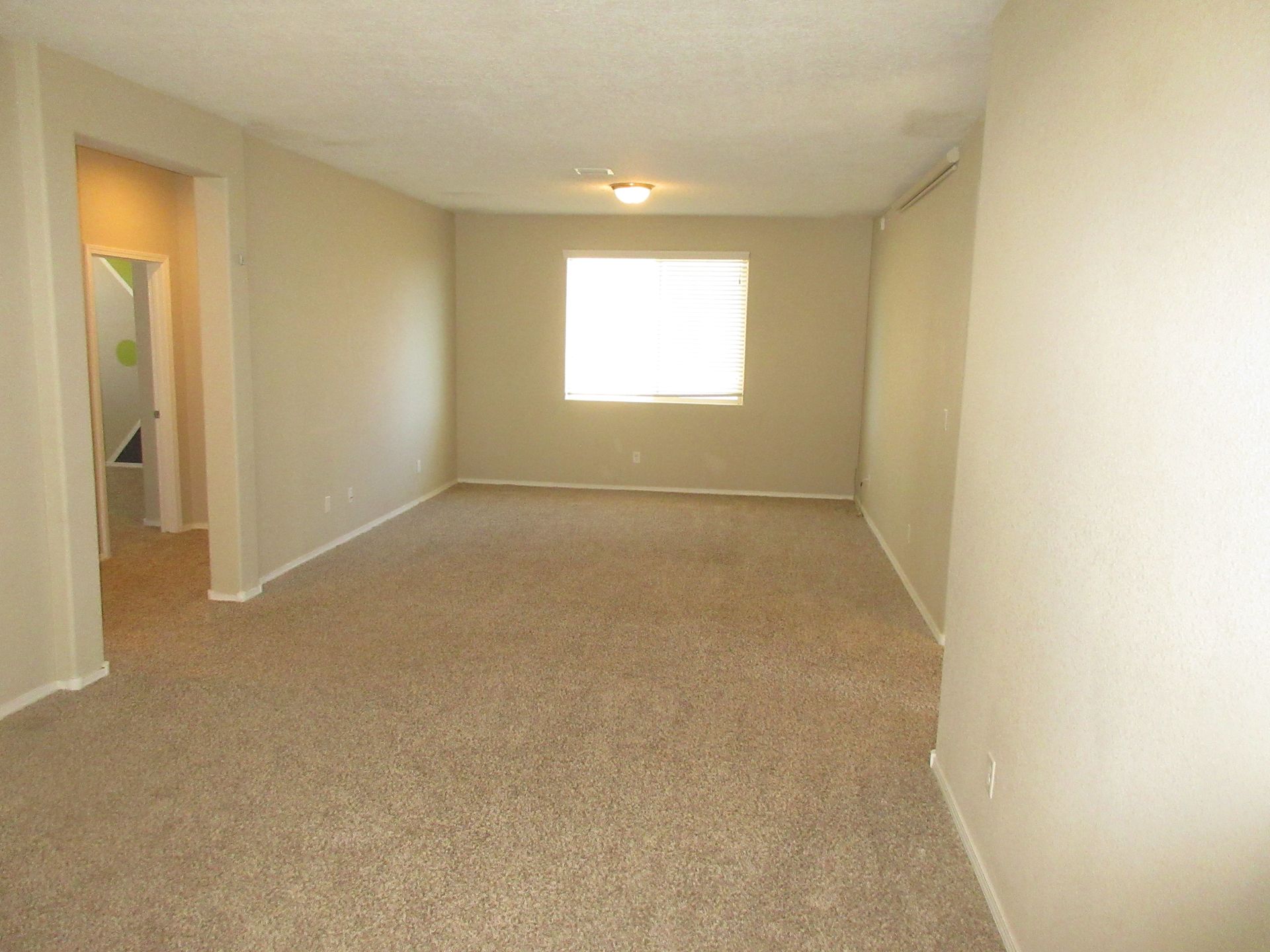 An empty living room with a window and carpet.