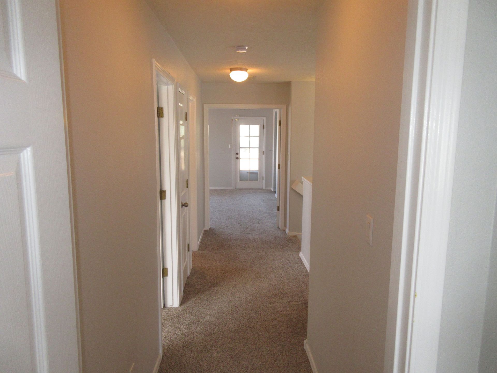 A hallway in a house with a carpeted floor and white walls.