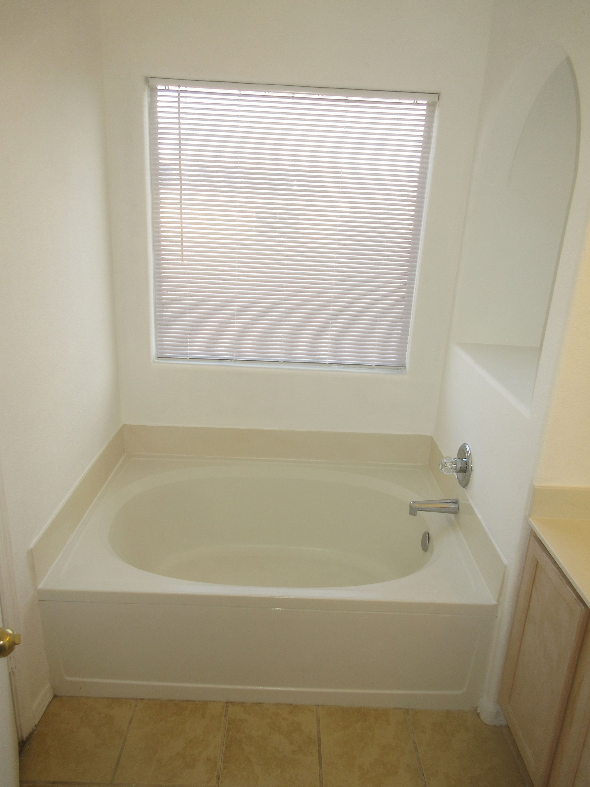 A bathroom with a bathtub and a window with blinds.