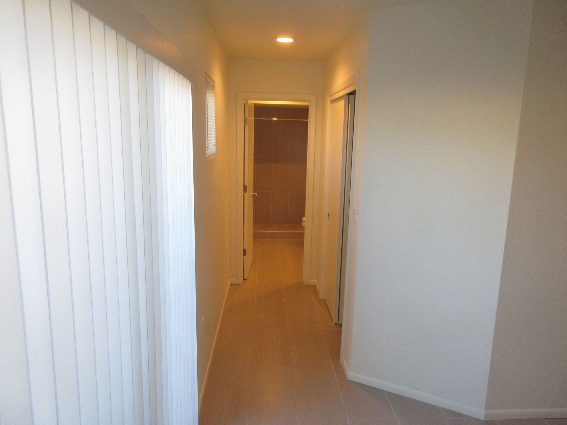 A long hallway with white walls and a window leading to a bathroom.