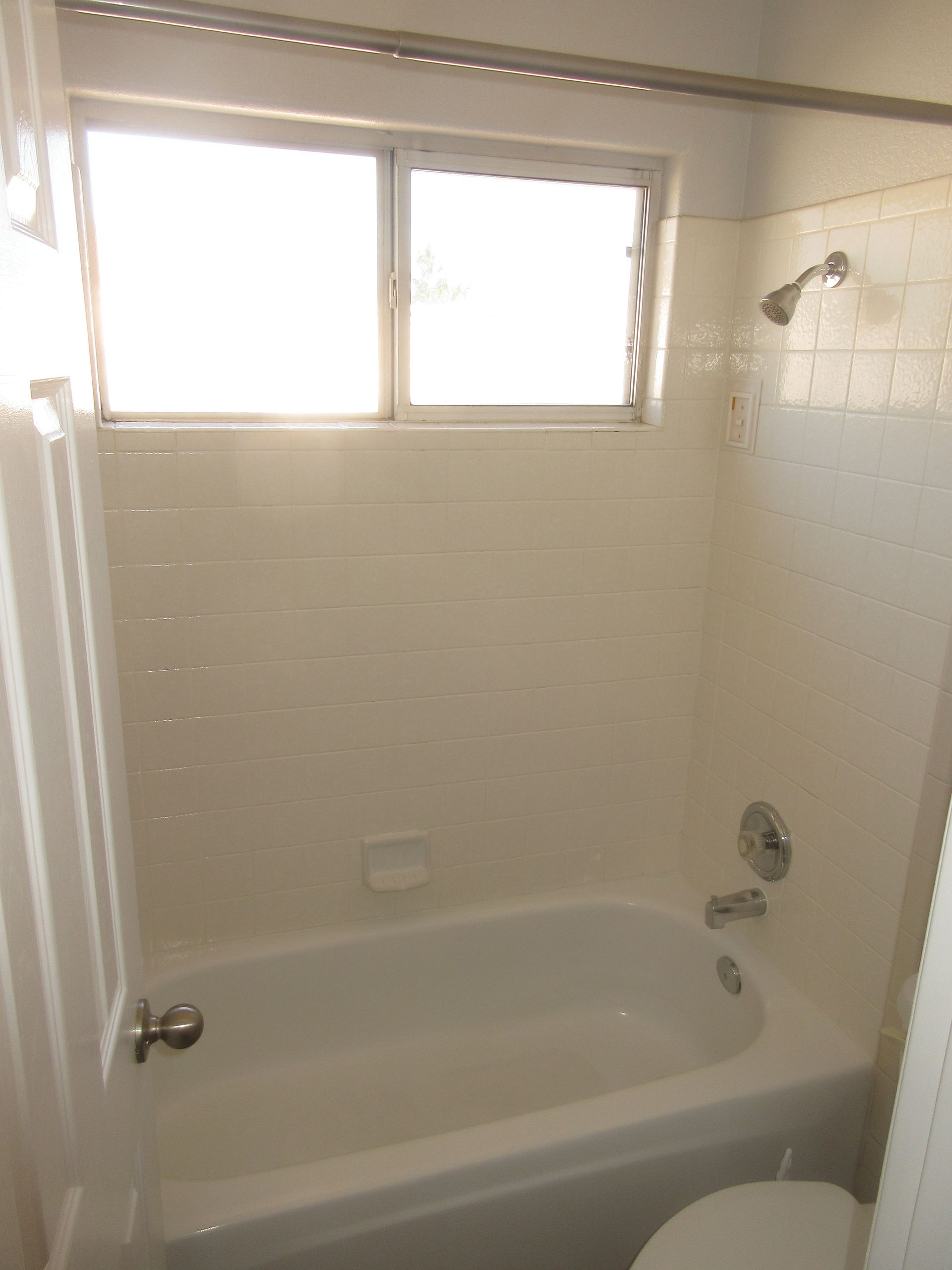 A bathroom with a tub , toilet , shower and window.