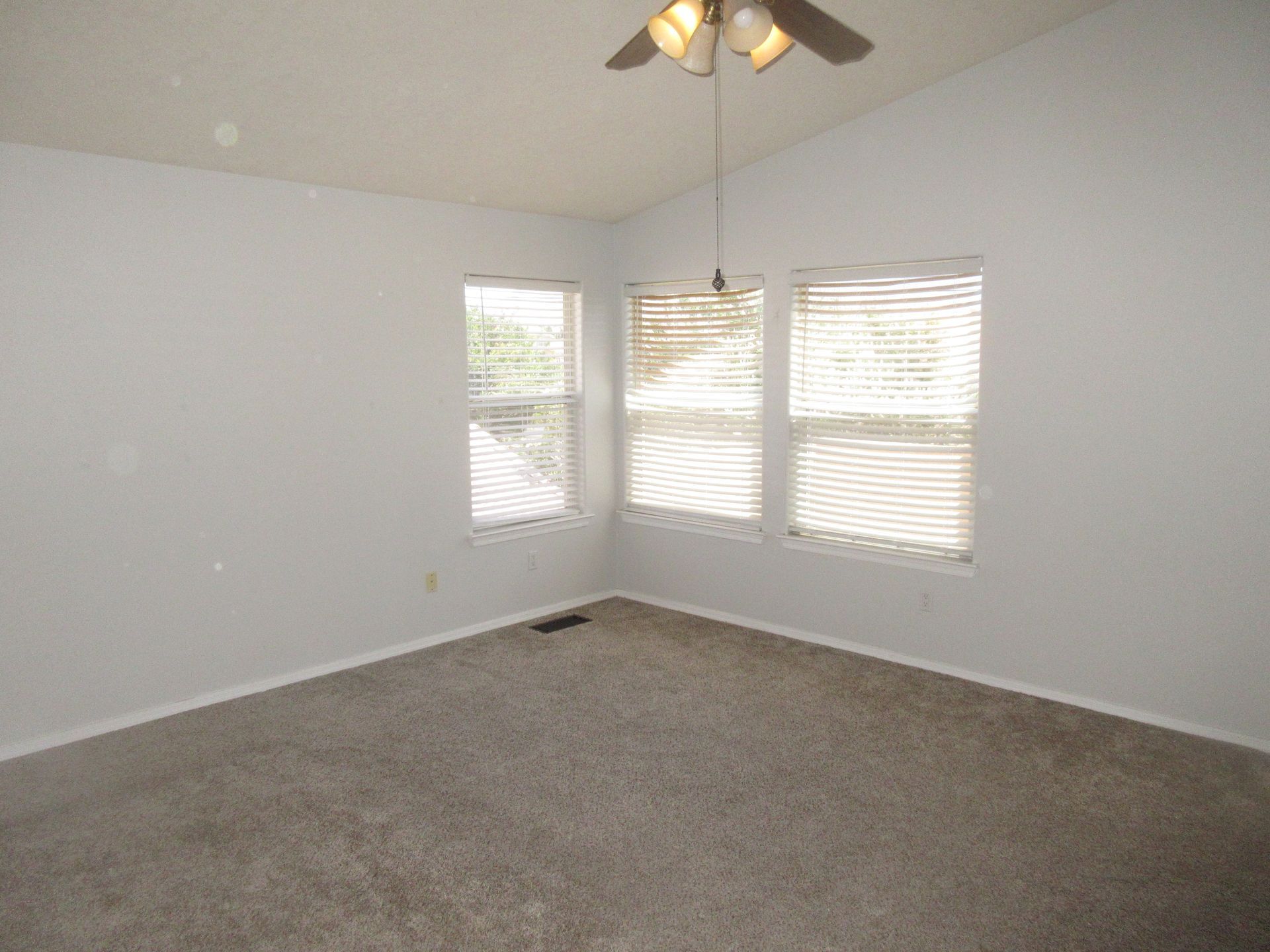 An empty bedroom with a ceiling fan and three windows.
