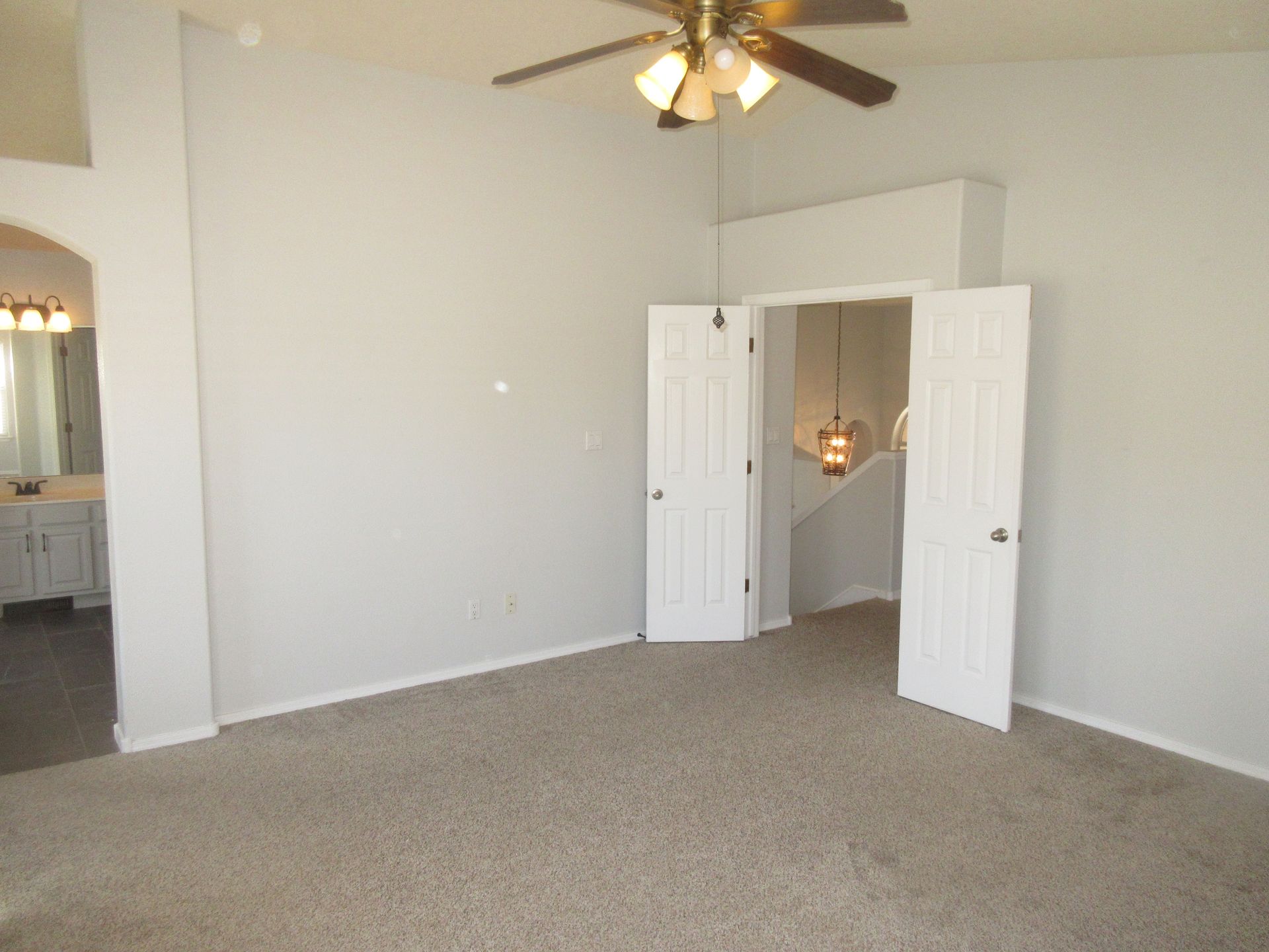 An empty bedroom with a ceiling fan and white doors