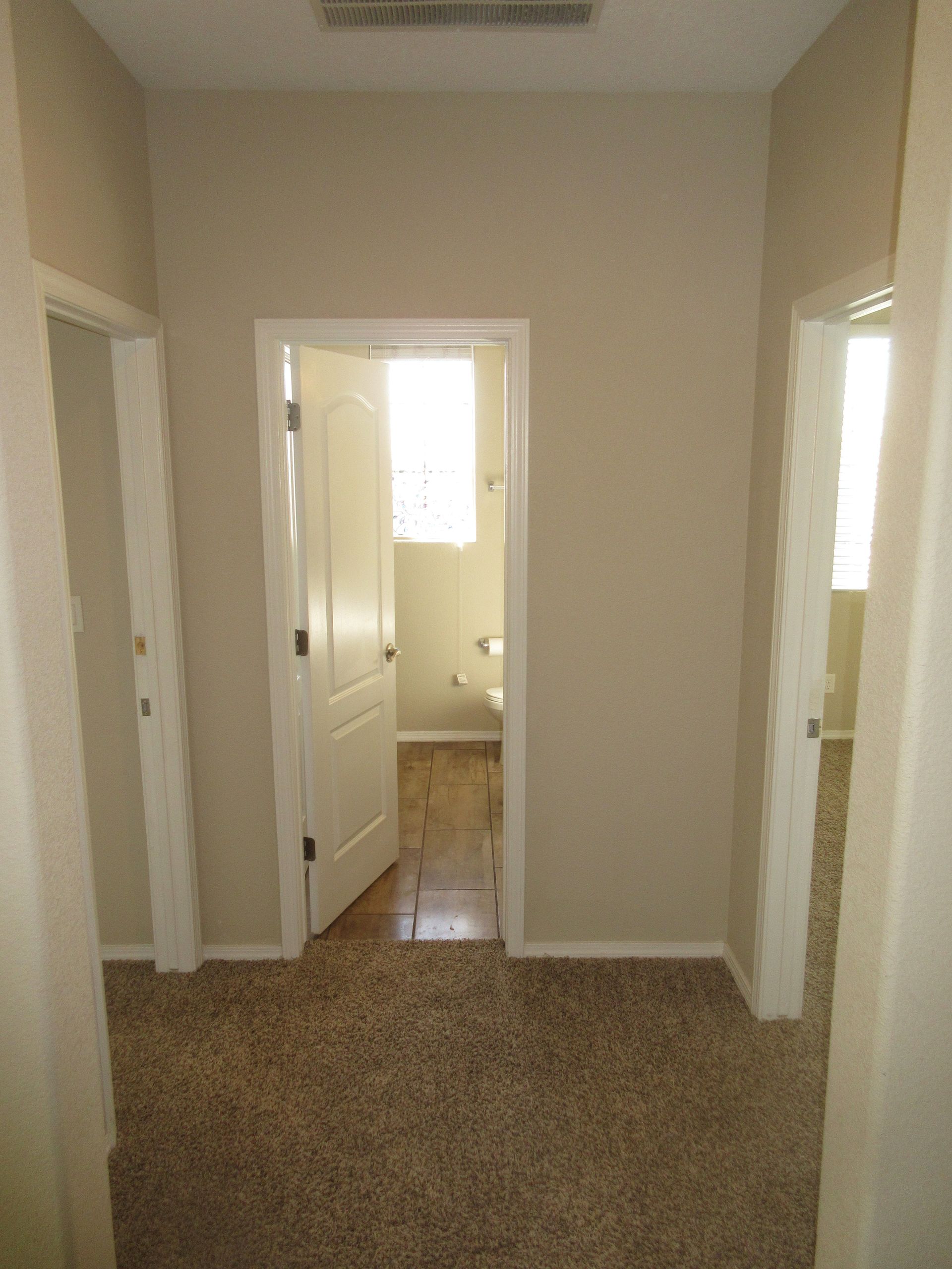 A hallway with a carpeted floor and a door leading to a bathroom.