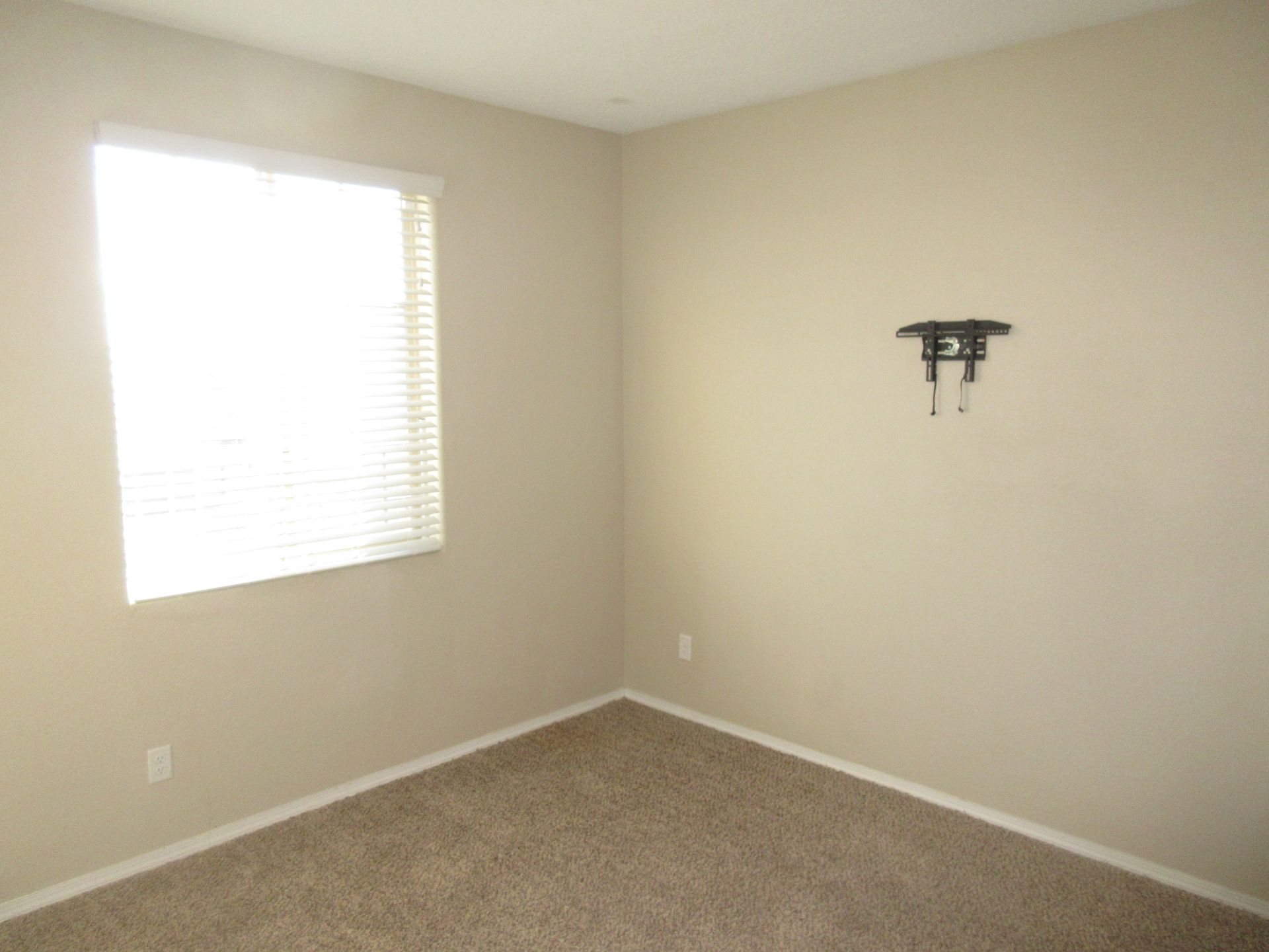 An empty bedroom with a window and a flat screen tv mounted on the wall.