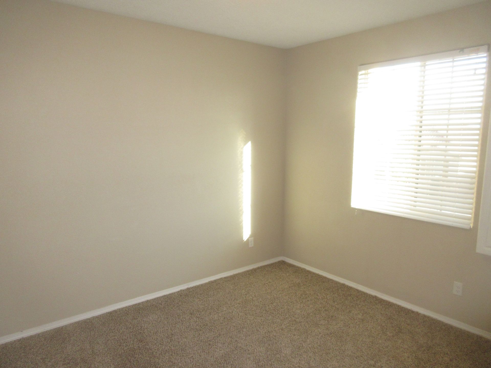 An empty bedroom with a window and blinds.