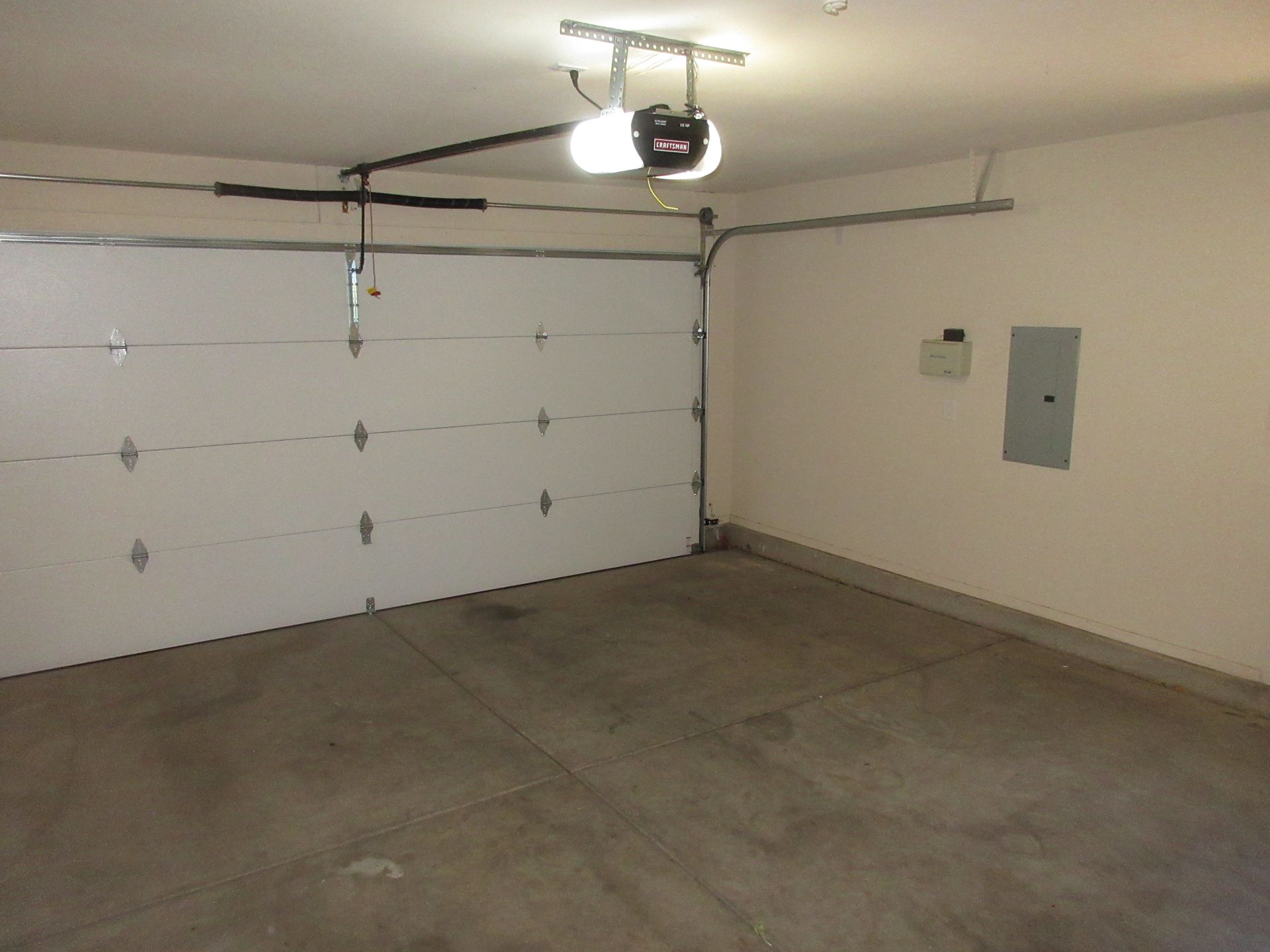 An empty garage with a garage door open and a light on the ceiling.
