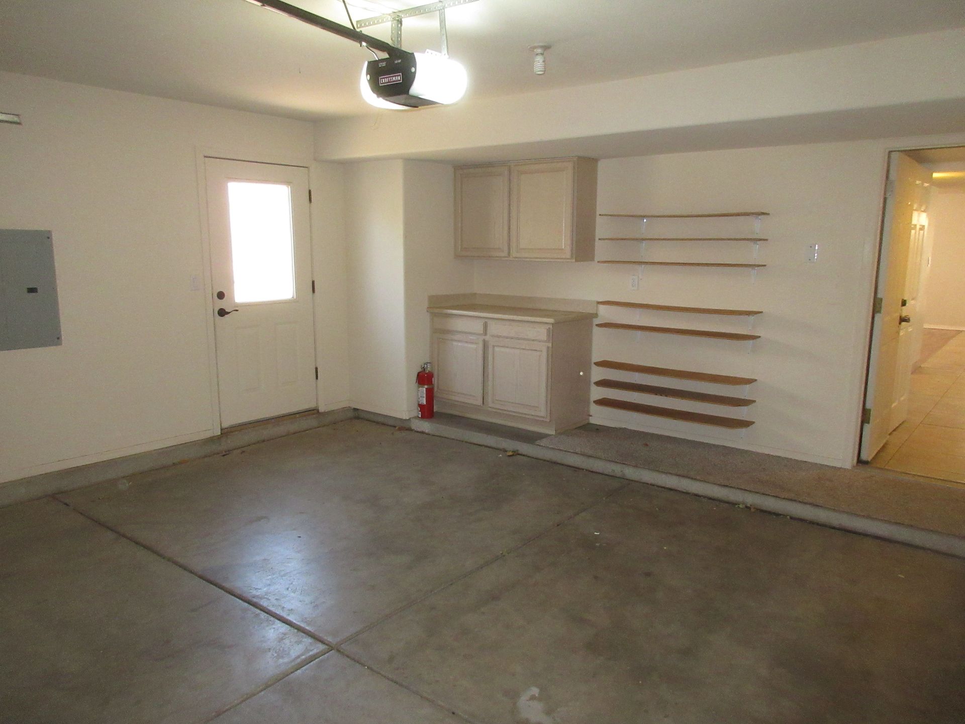 An empty garage with a garage door open and a fire extinguisher on the wall.