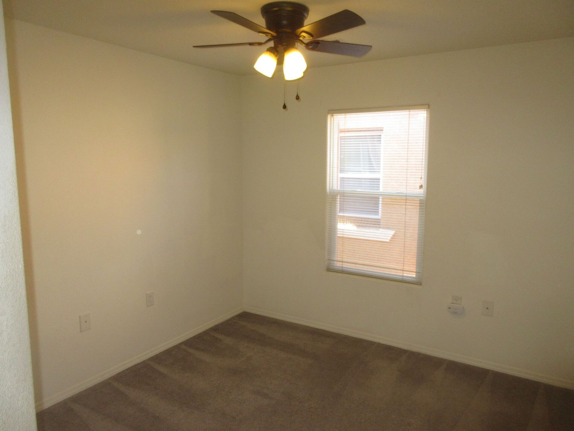 An empty bedroom with a ceiling fan and a window.