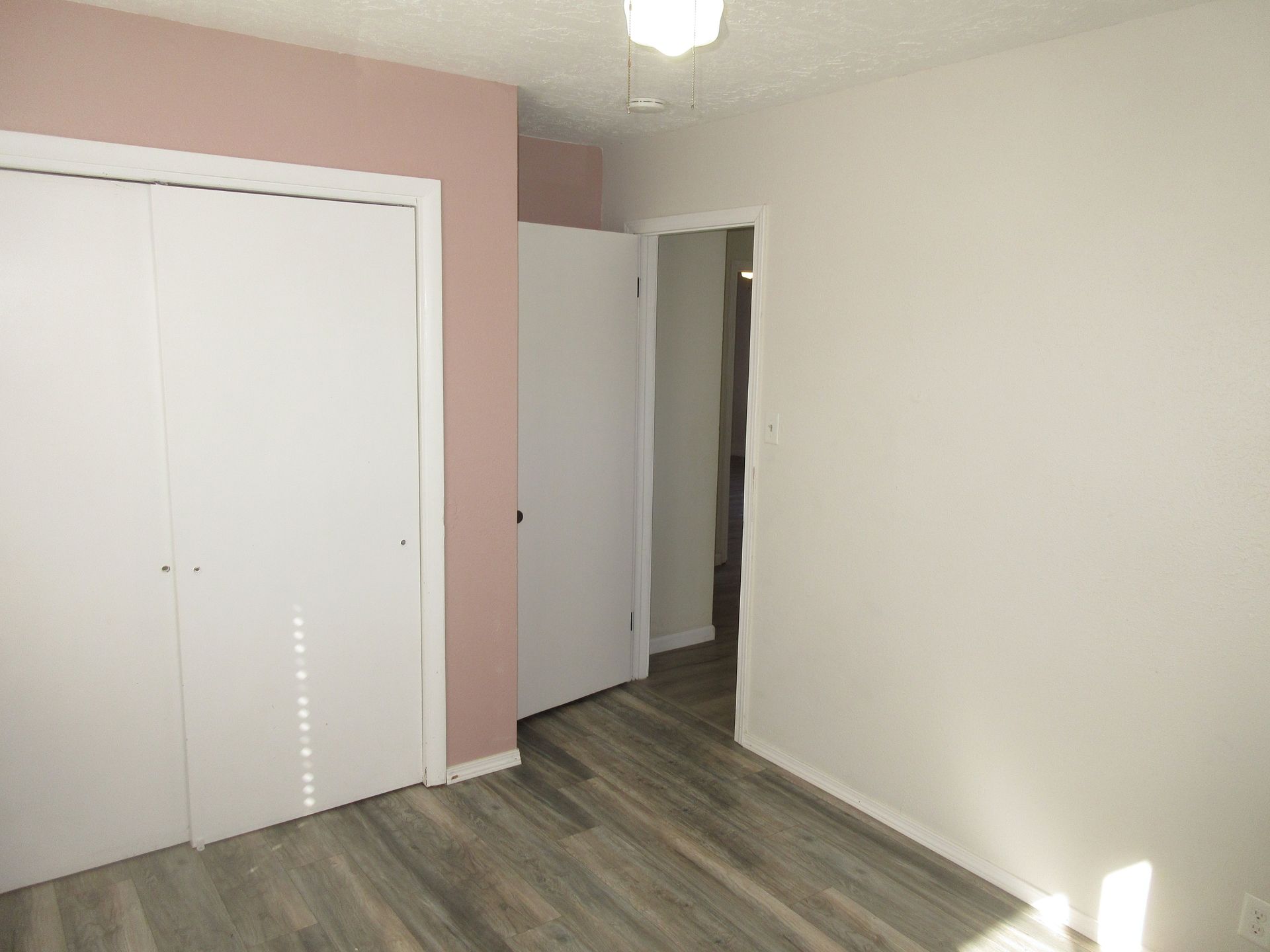 An empty bedroom with pink walls and white closet doors.
