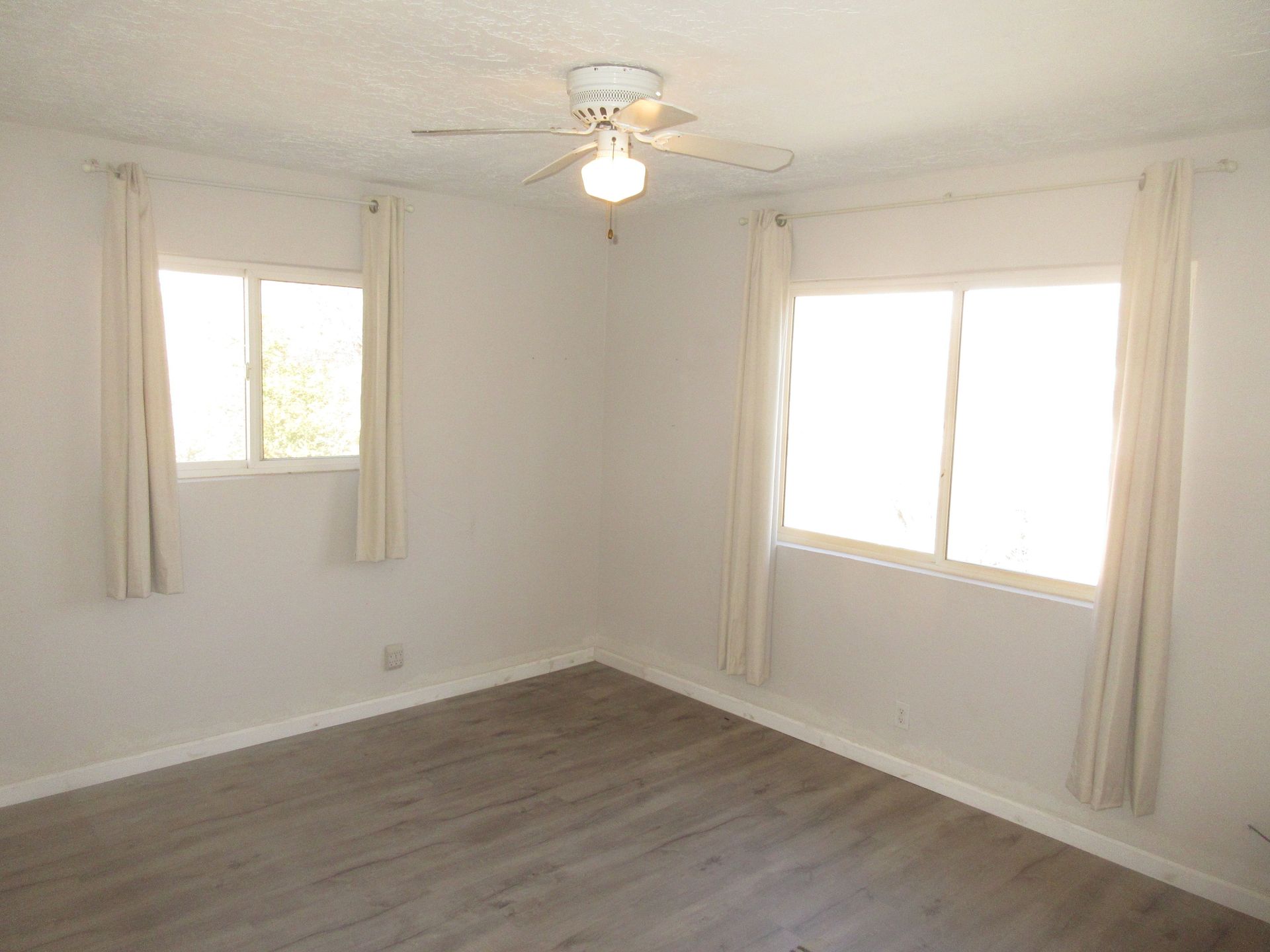 An empty room with a ceiling fan and two windows.
