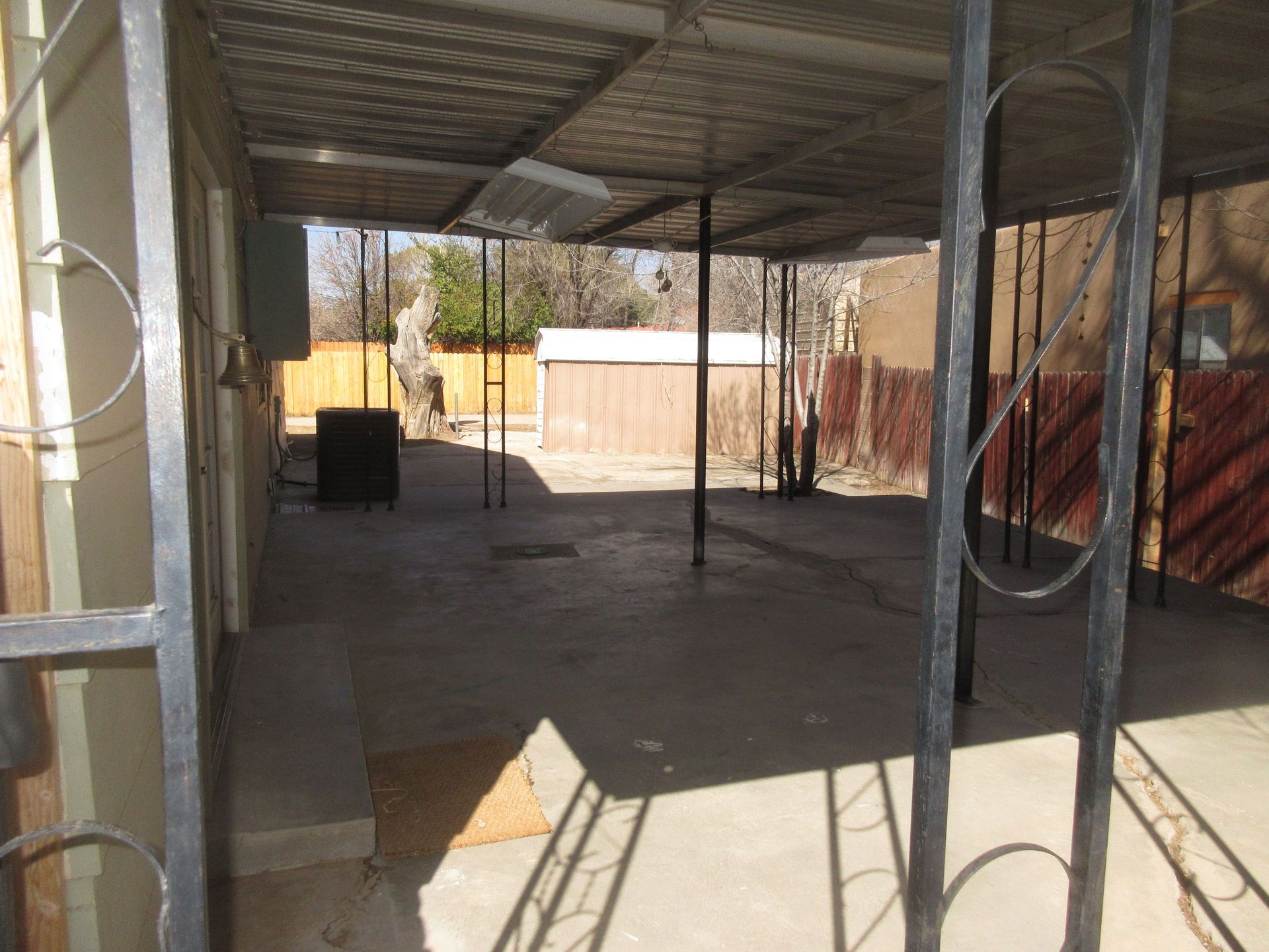 A metal fence surrounds a covered area with a shed in the background