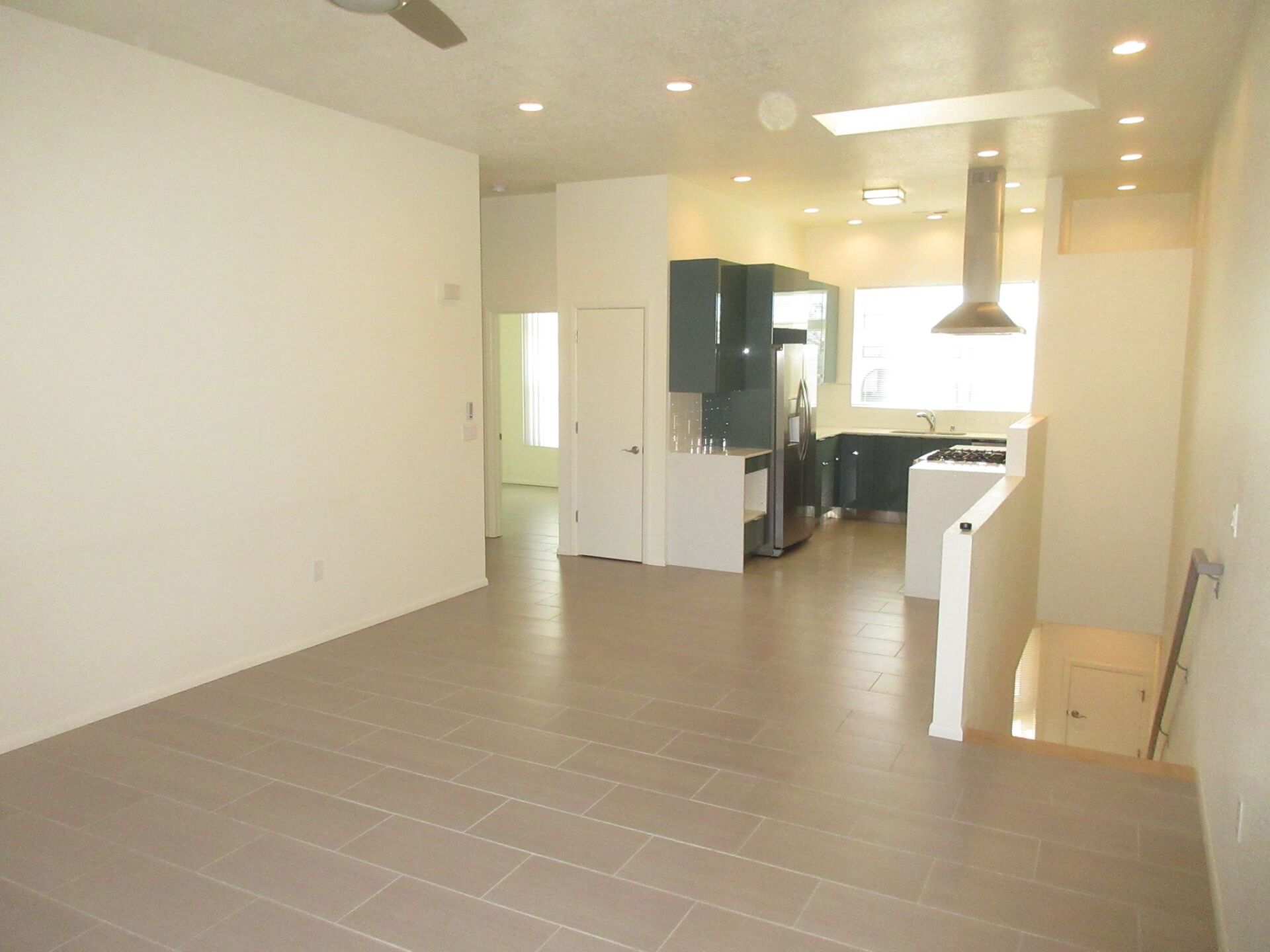 A living room with a ceiling fan and a kitchen in the background