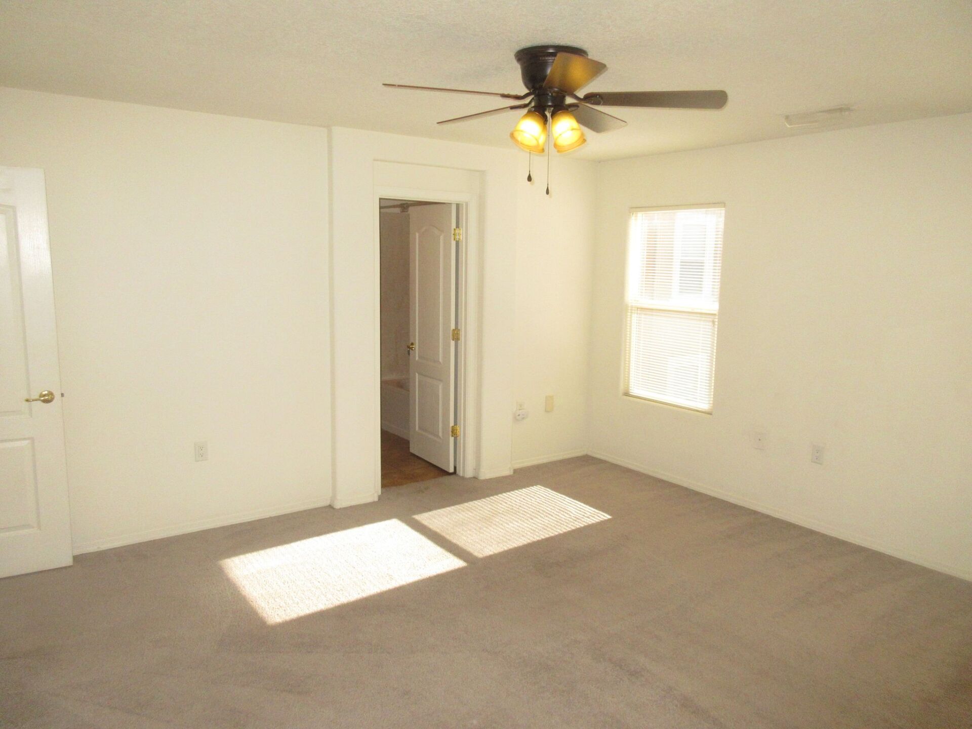 An empty bedroom with a ceiling fan and a window