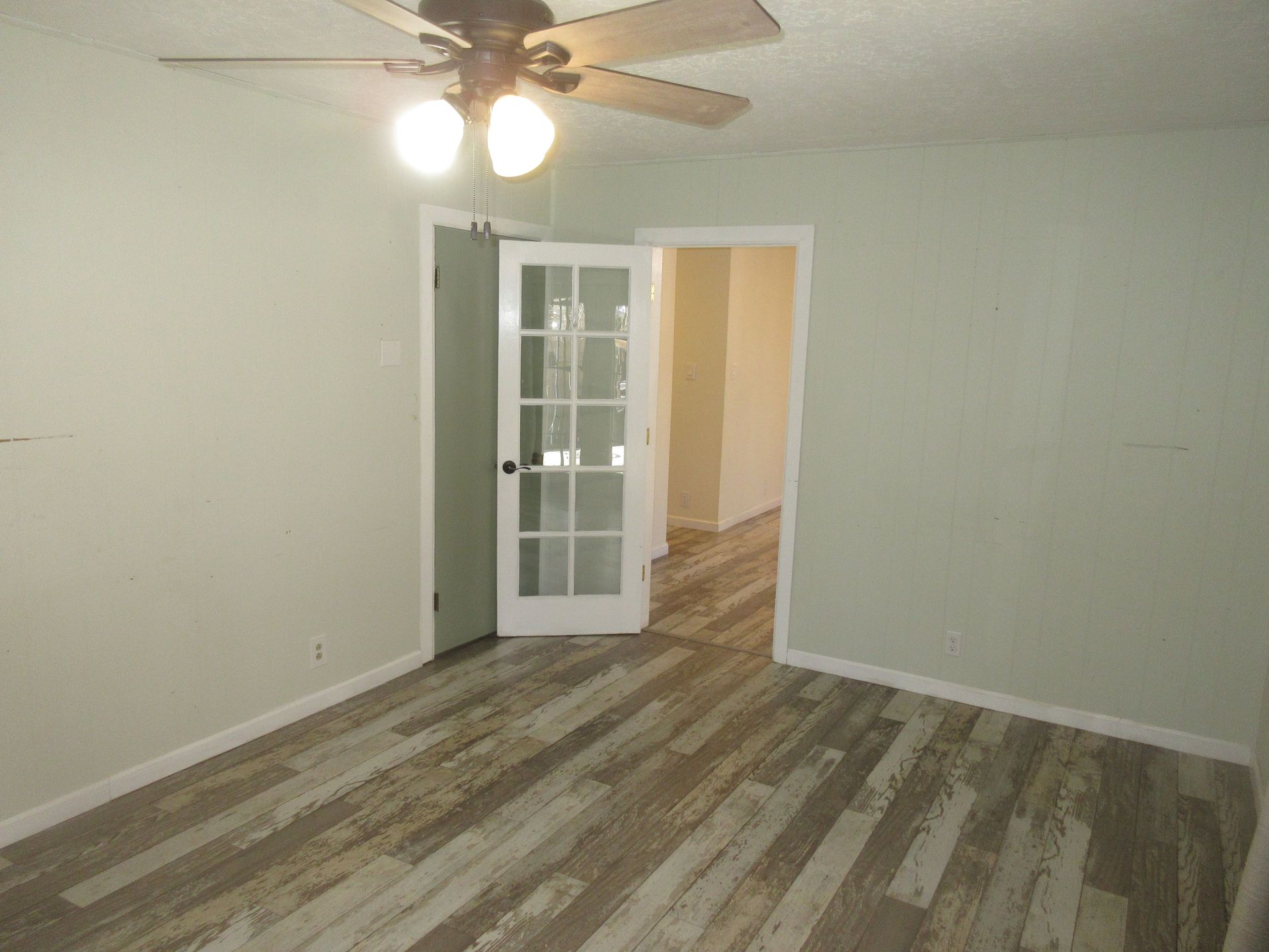 An empty room with a ceiling fan and a french door.