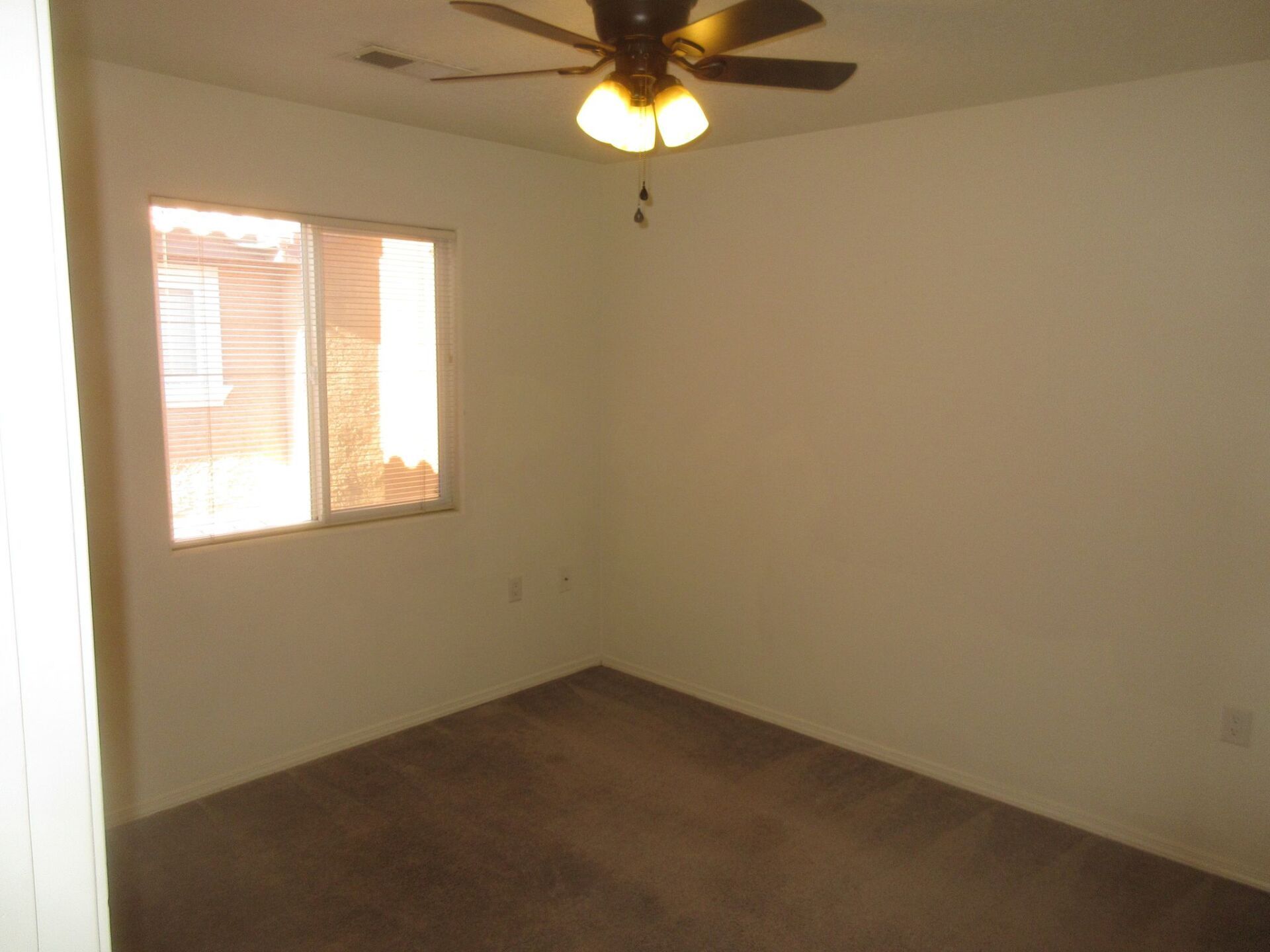 An empty bedroom with a ceiling fan and a window.