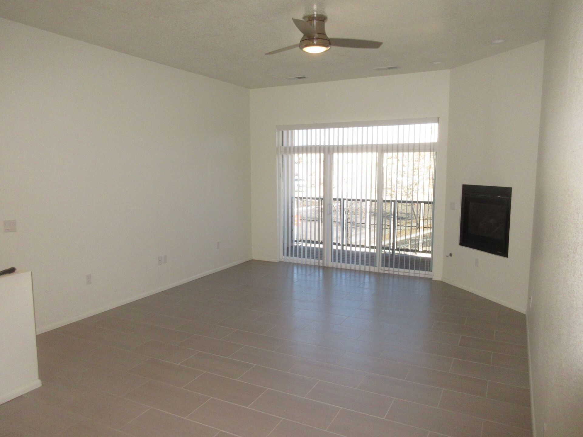 An empty living room with a ceiling fan and sliding glass doors