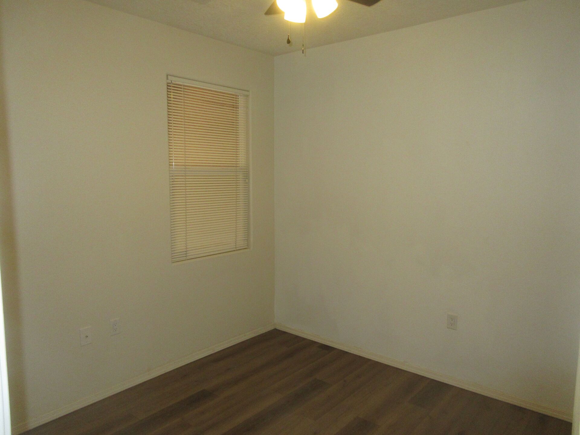 An empty bedroom with a window and a ceiling fan.
