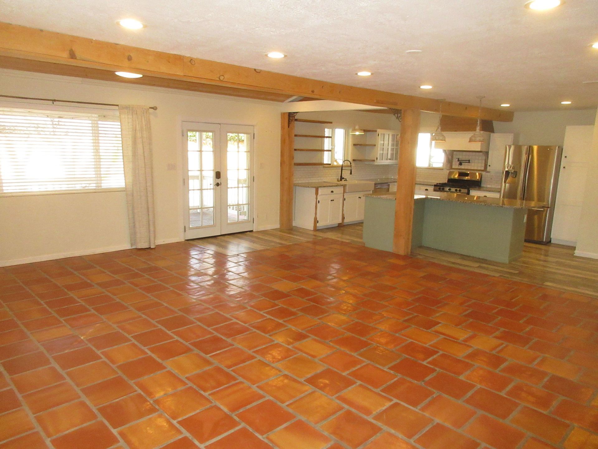 An empty room with a tiled floor and a kitchen in the background