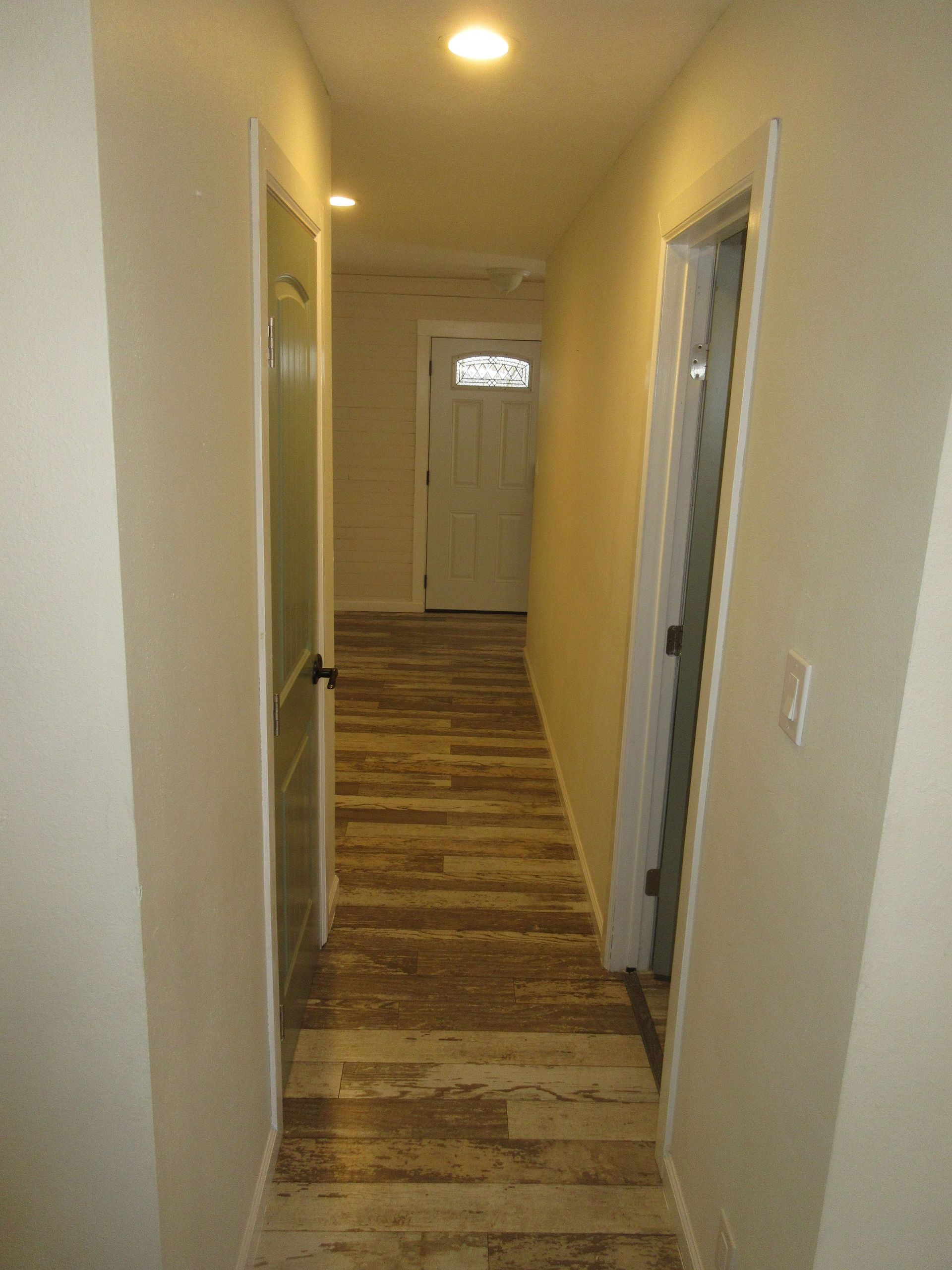 A long hallway with wooden floors and white walls leading to a door.
