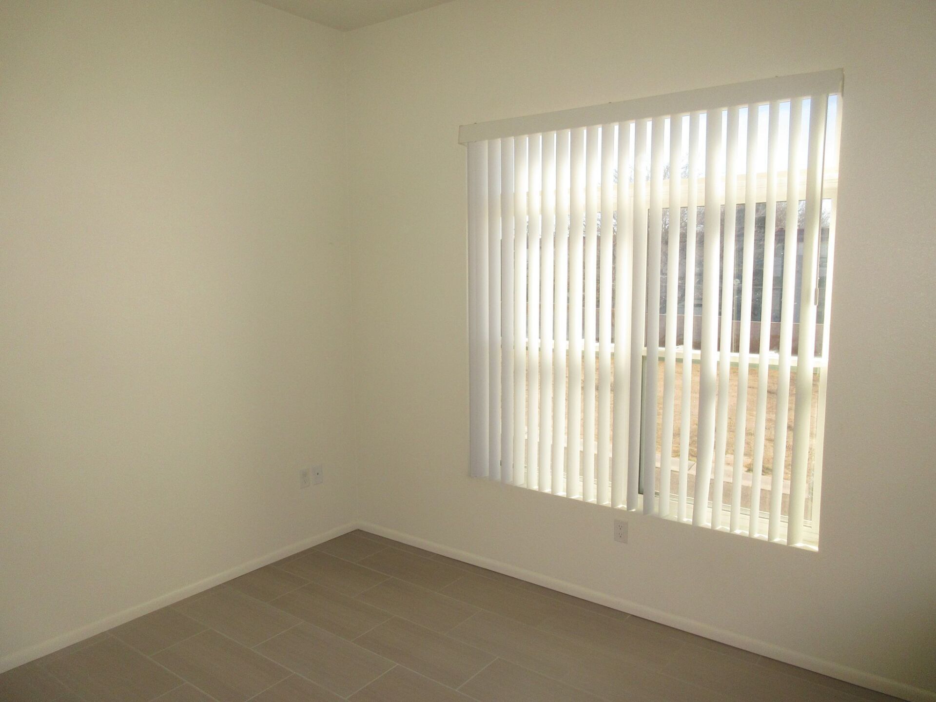 An empty room with a sliding glass door and vertical blinds